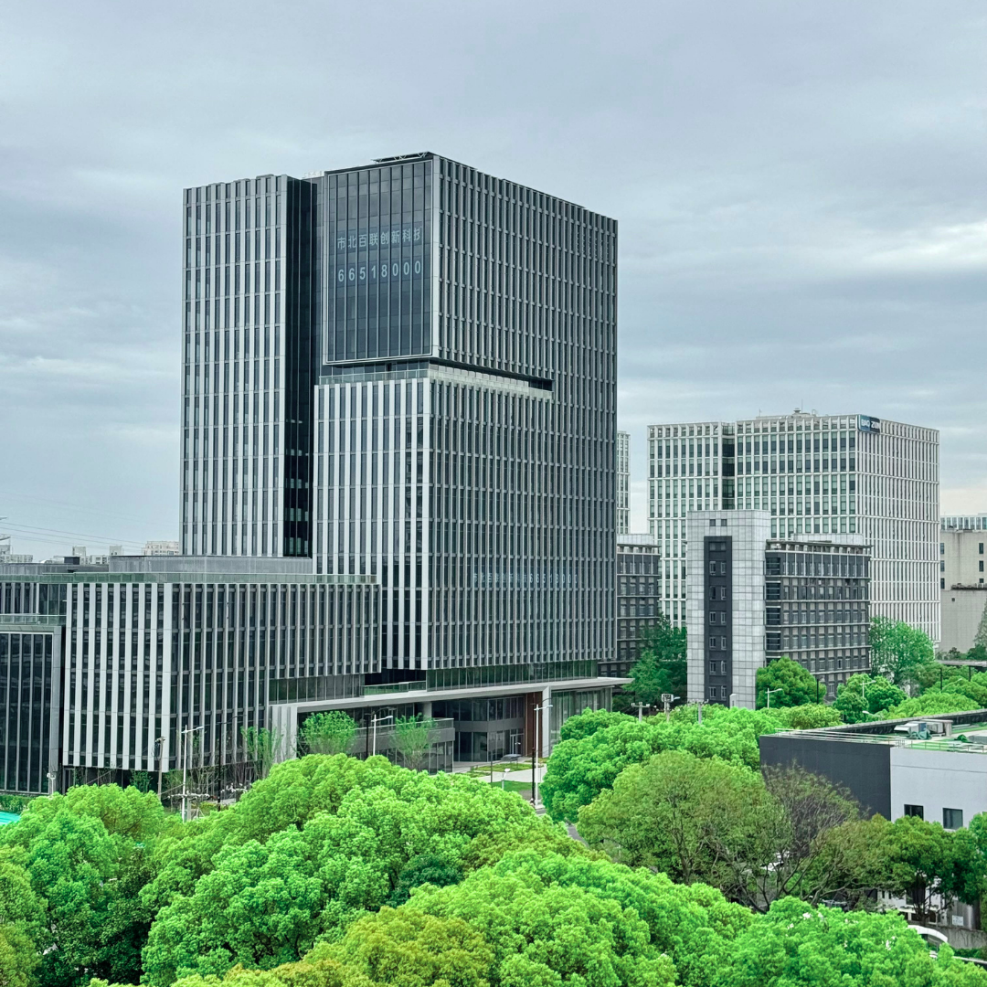Photo of modern office buildings surrounded by green trees on an overcast day.