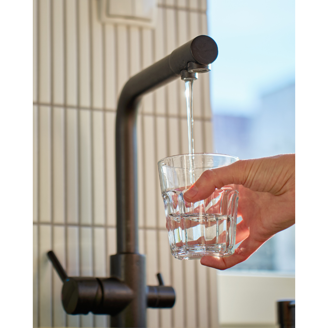 A person holding a glass under a stainless steel faucet, filling it with water in a kitchen or similar setting.