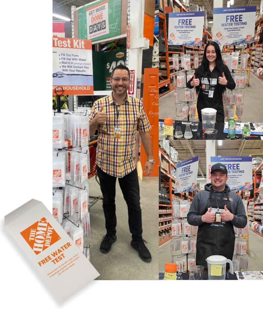 Three people at a home improvement store sampling water testing kits. The man on the left is wearing a plaid shirt, smiling, giving a thumbs up. The woman in the middle and the man on the right are standing at tables with water testing supplies, also giving thumbs up. Signage displays for free water testing kits are visible in the background.