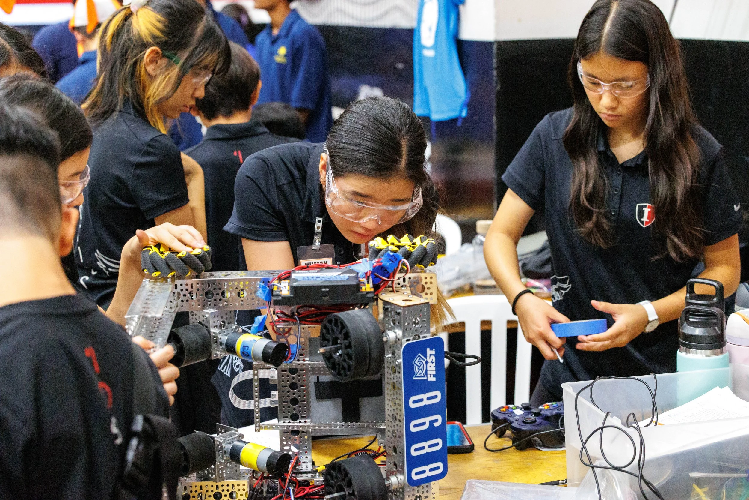 Group of students working together on a robotics project at a competition or workshop, with various electronic components and tools around them.