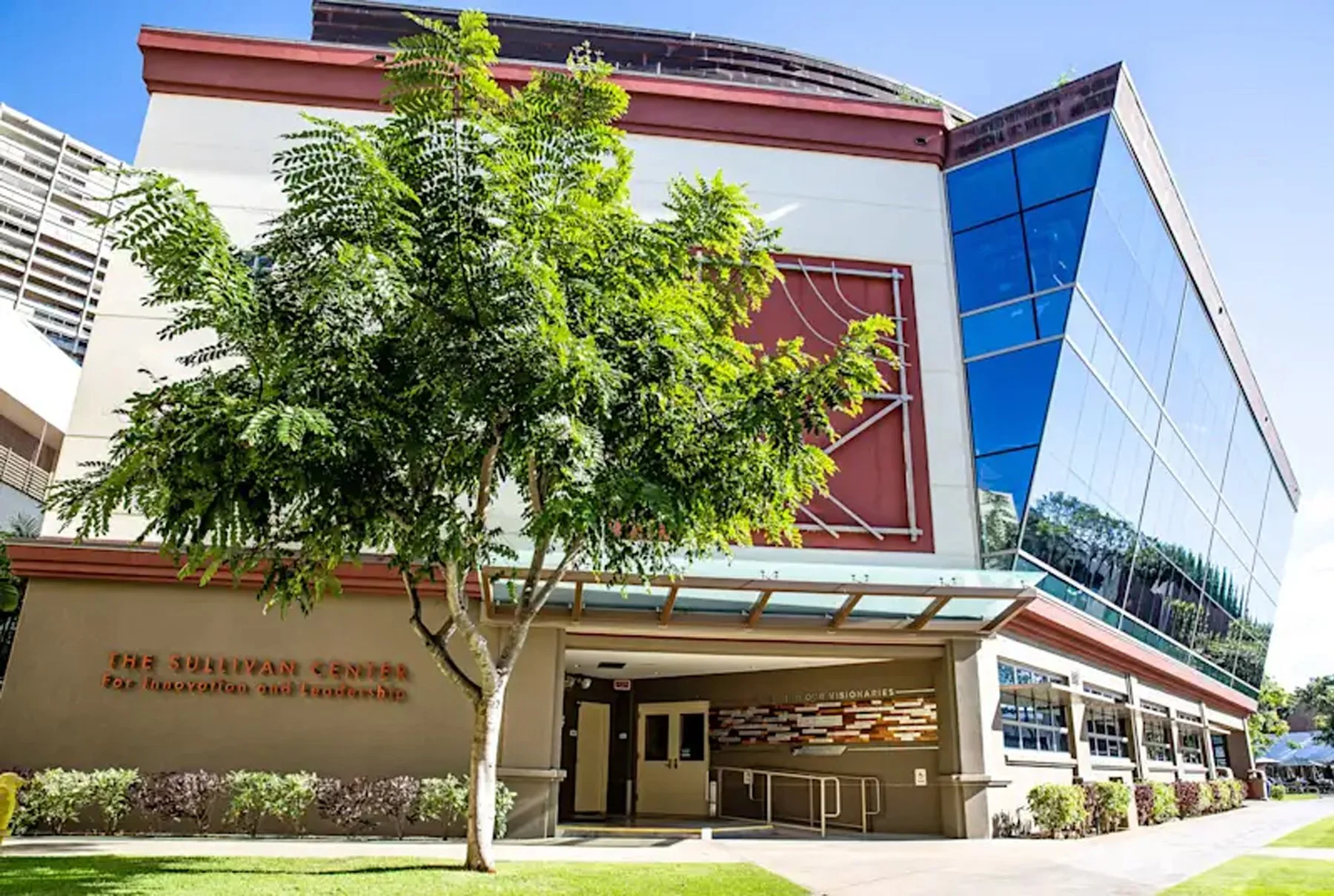 The Sullivan Center, a modern building with a glass facade and red accents, featuring a set of stairs leading to the entrance, surrounded by a landscaped area with trees and bushes.