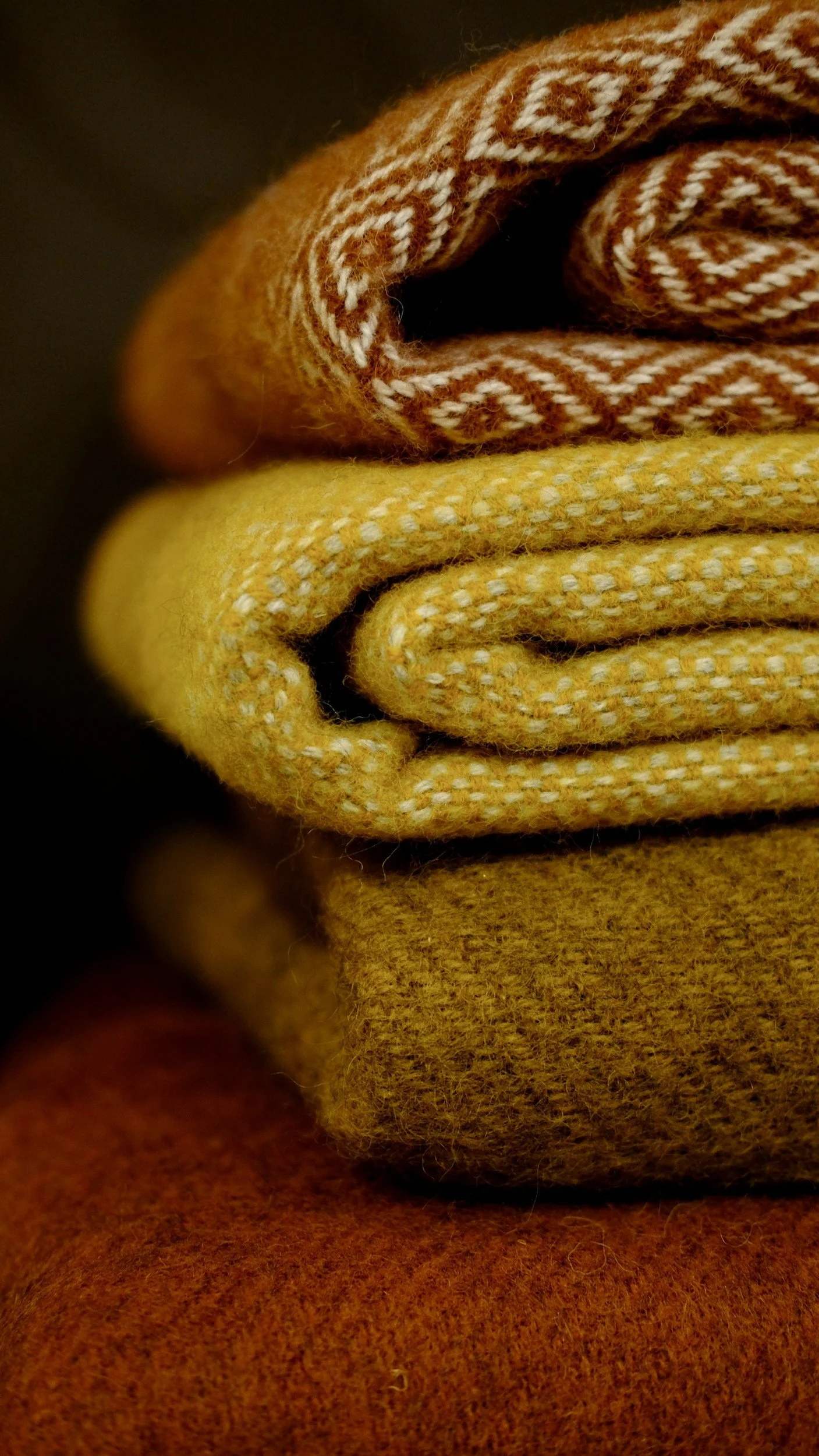 Stacked folded yellow, orange, and patterned fabric or wool clothing with a dark background.