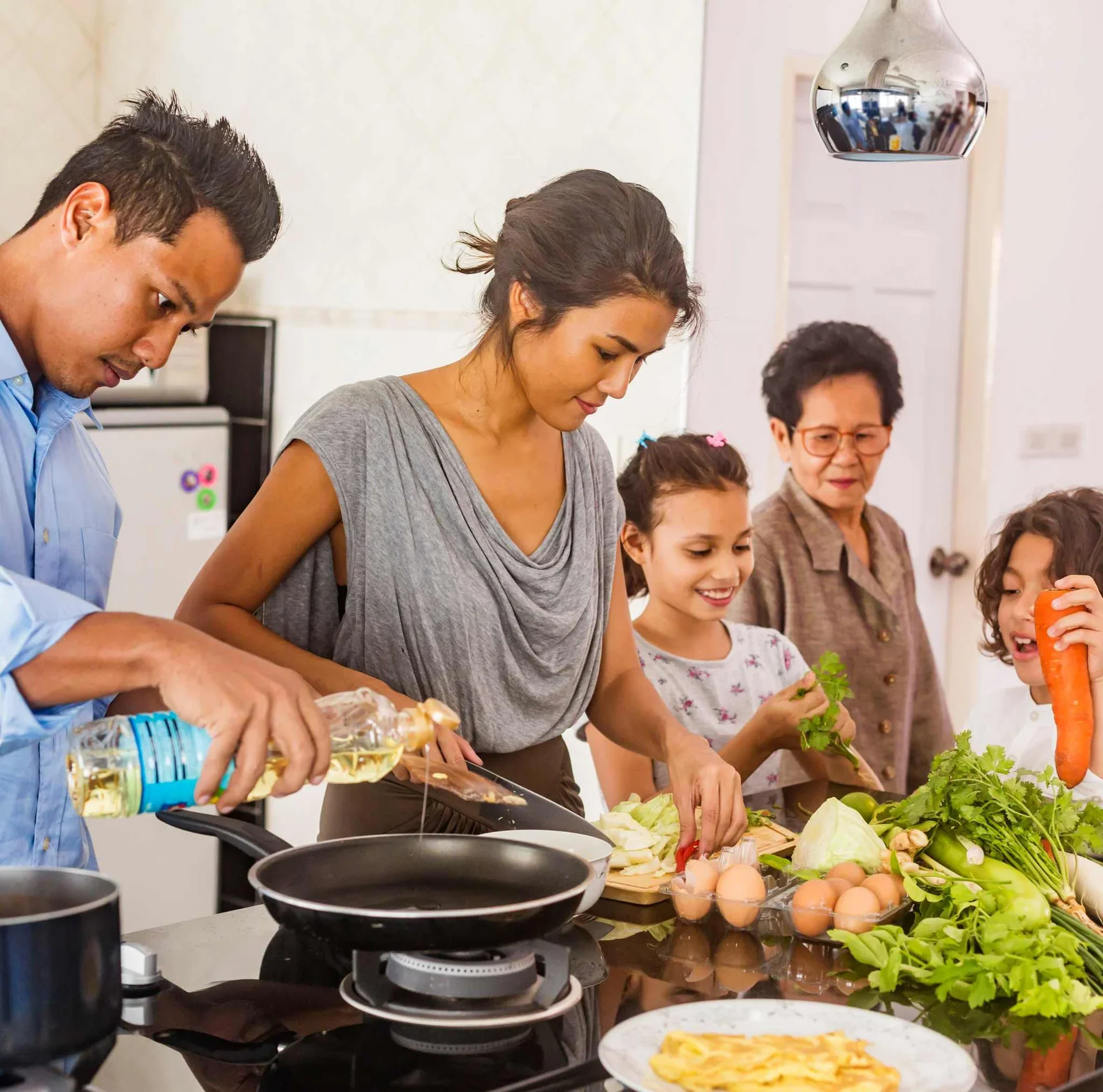 People preparing food in a kitchen, with vegetables, eggs, and cooking utensils on the counter.