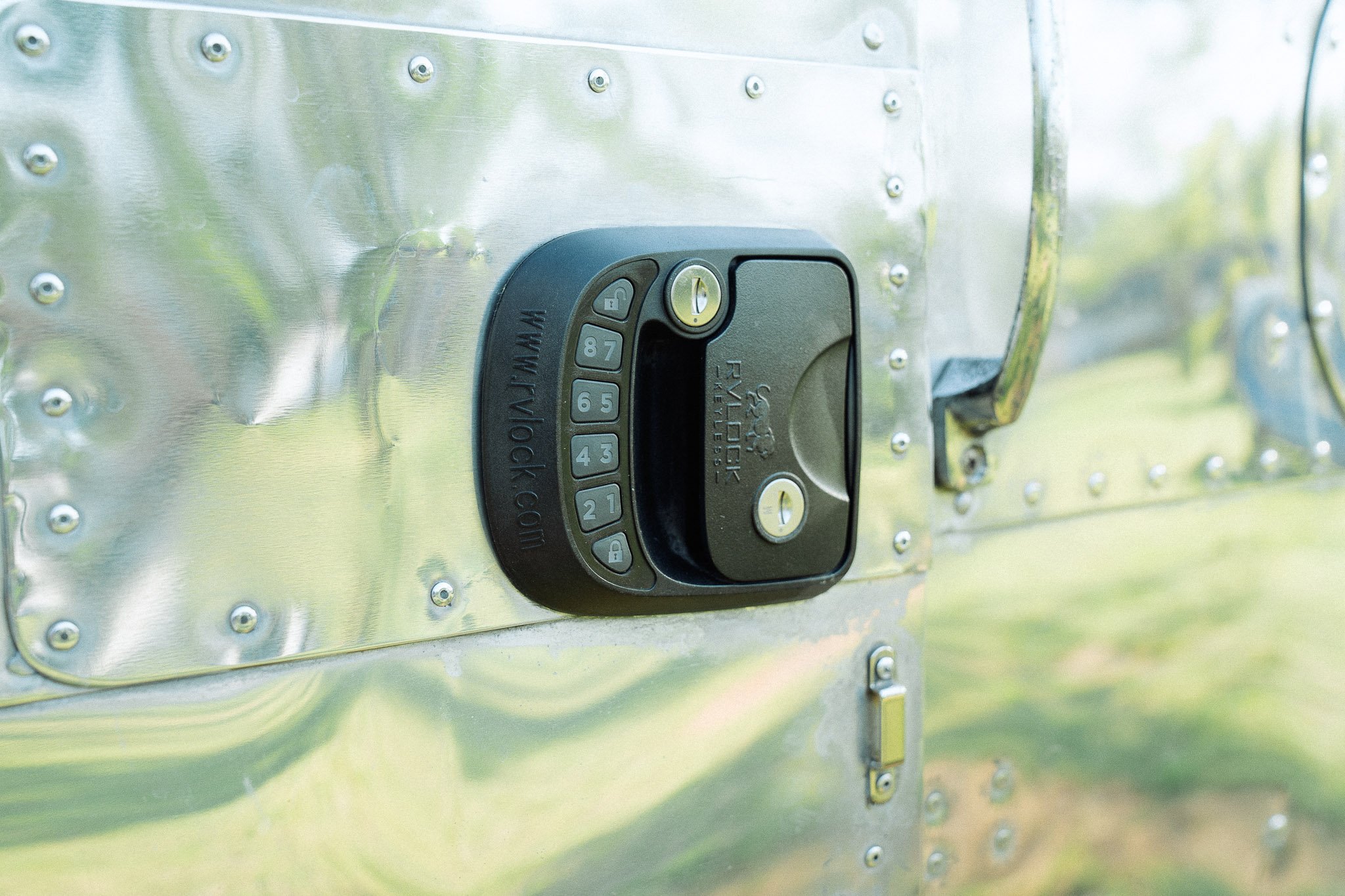 Close-up of a combination lock on a metallic surface, with a grassy outdoor background.