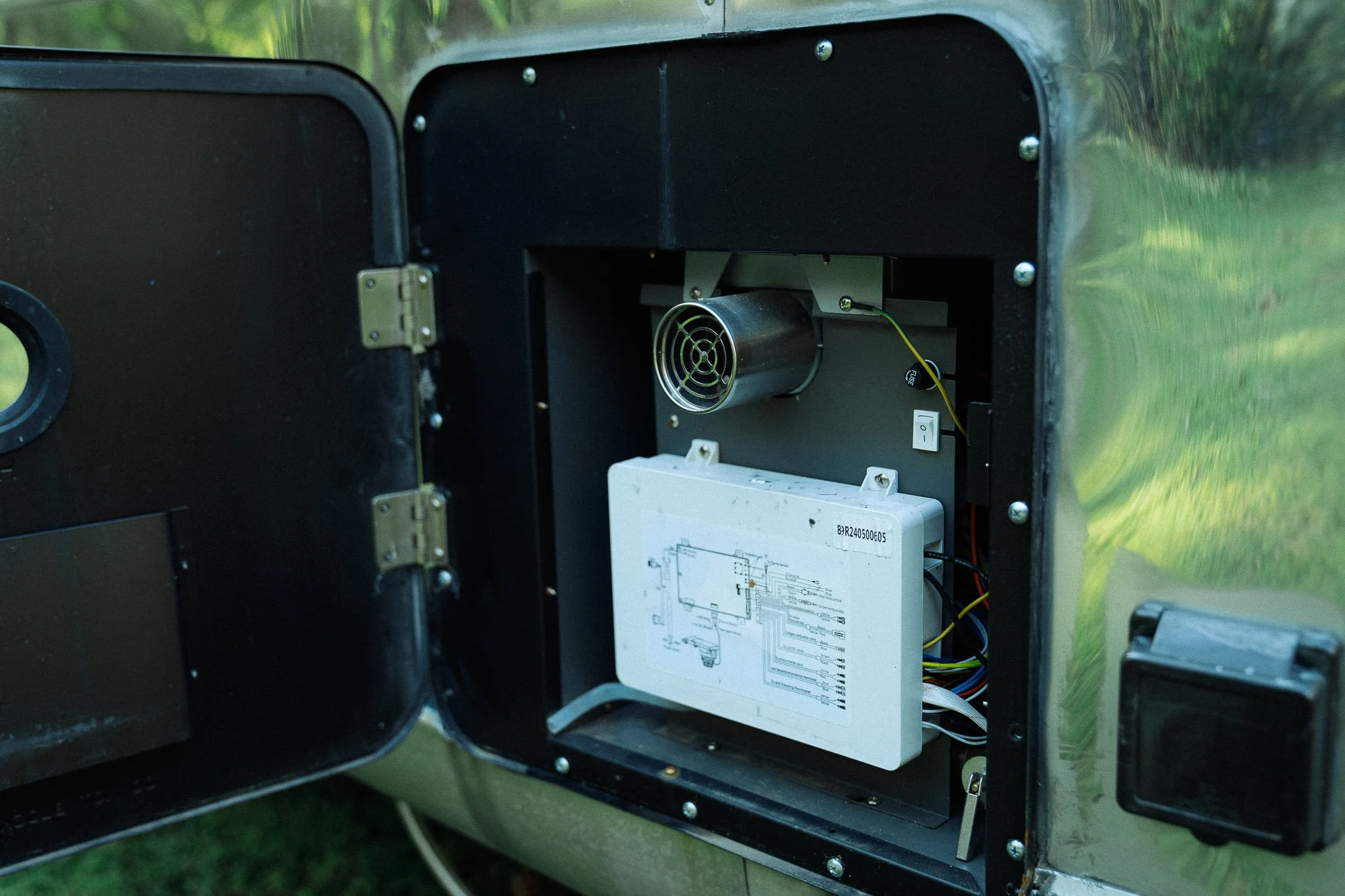 Open black metal enclosure with electronic components inside, including a white circuit board, wires, and a small cylindrical fan at the top.
