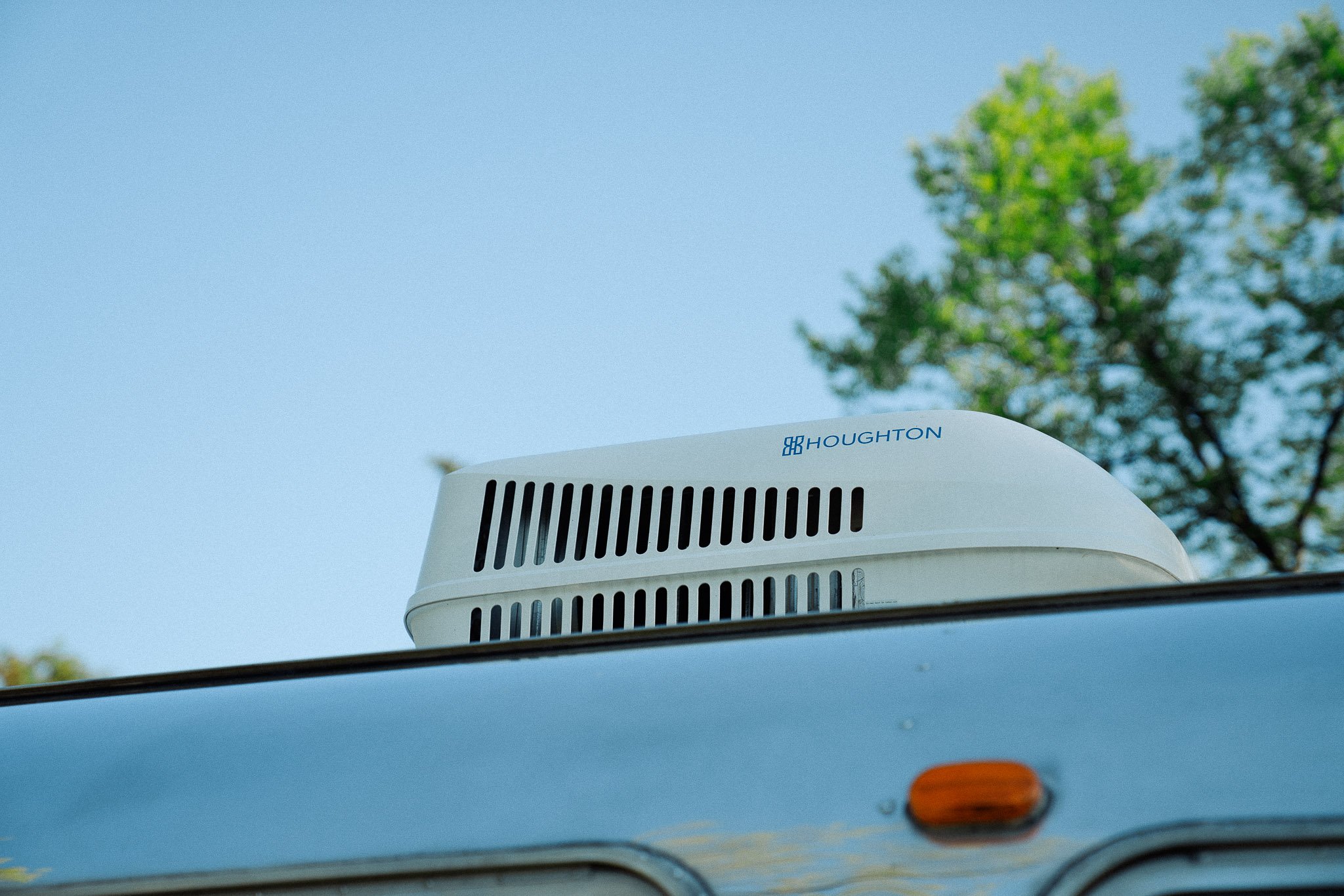 Close-up of a Houghton cooling tower or industrial equipment mounted on the roof of a vehicle, with trees and blue sky in the background.