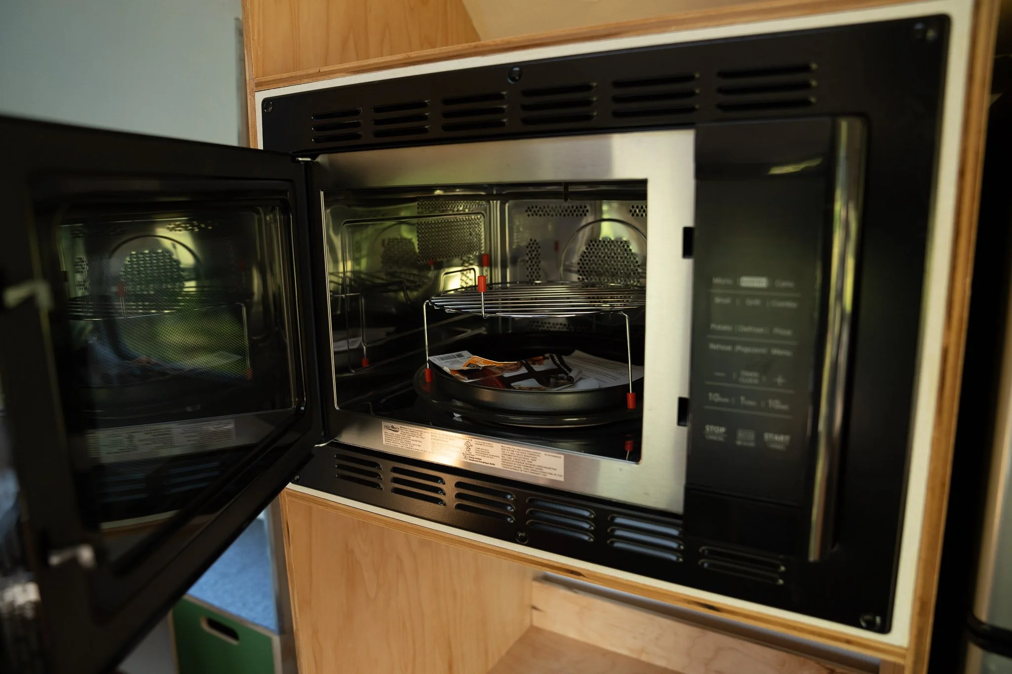 An open microwave oven built into a kitchen cabinet with some packaged food inside.