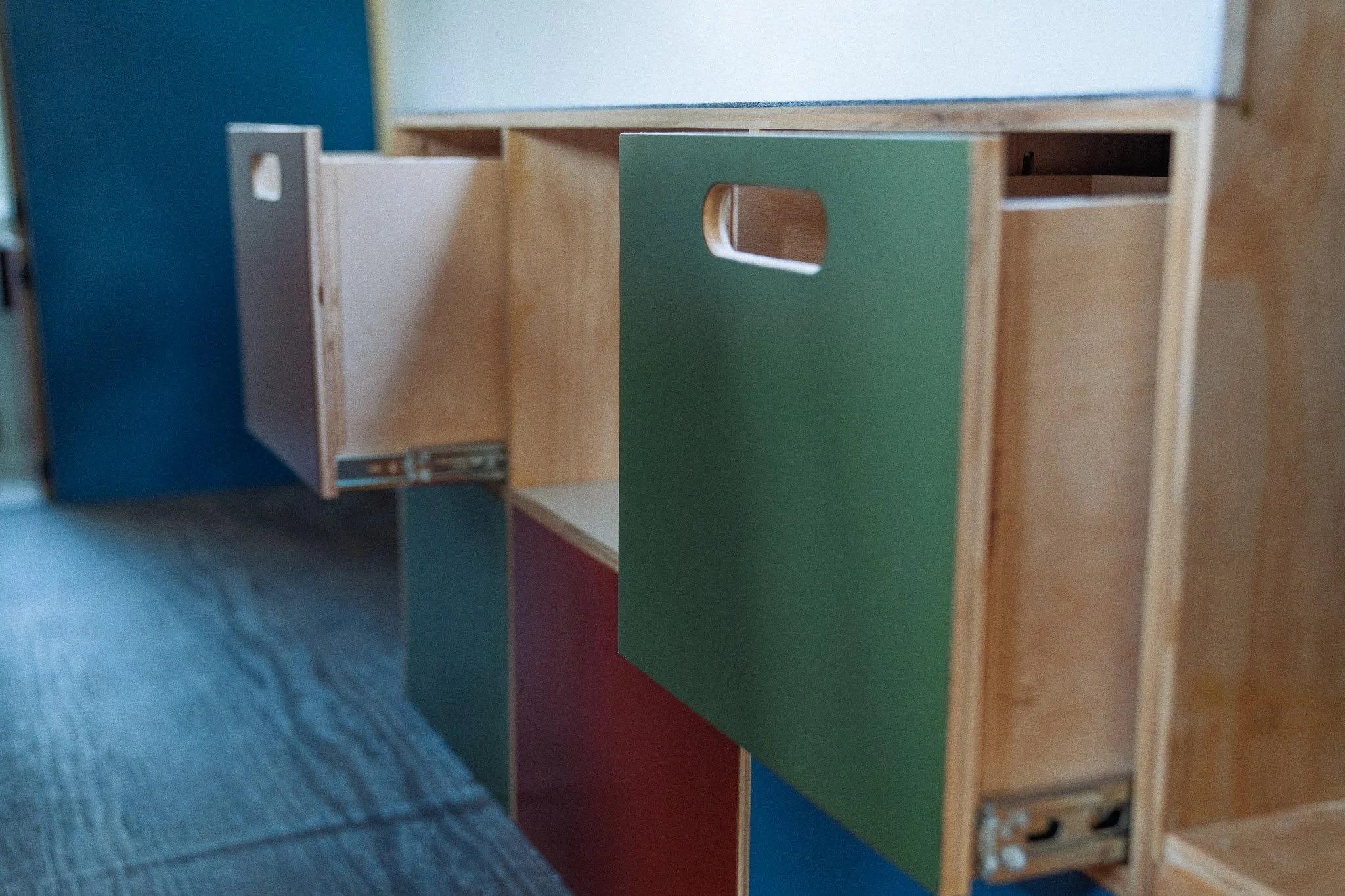 Wooden shelving unit with colorful panels, including green and red doors, located indoors on a carpeted floor.