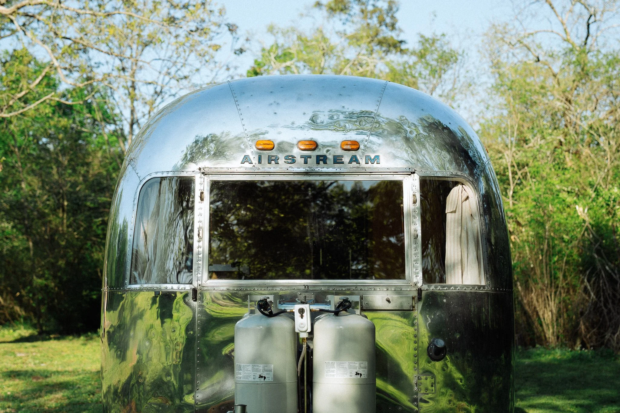 Front view of a shiny, metallic Airstream travel trailer parked outdoors with trees and grass in the background.