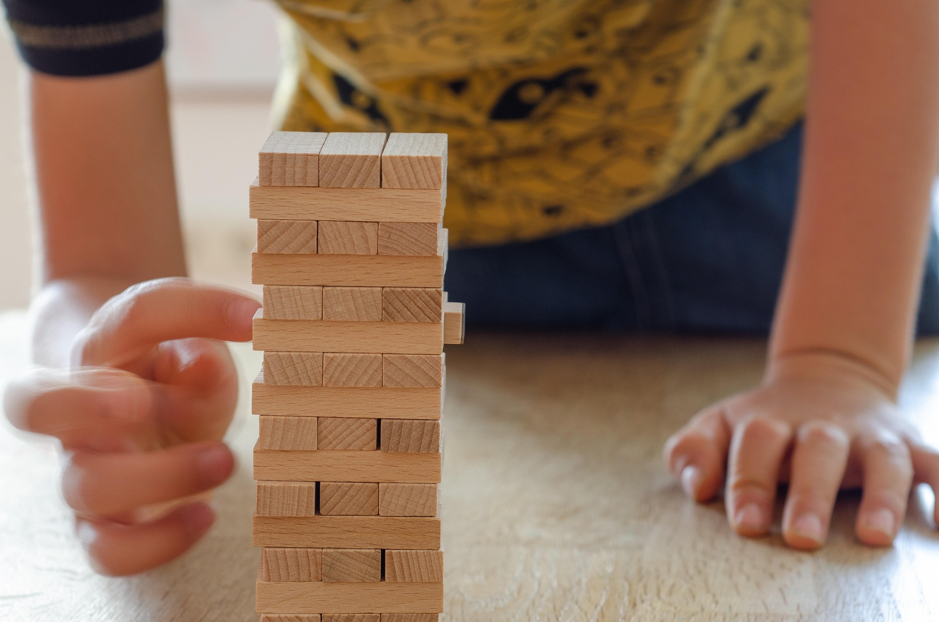 Close-up of a person playing a game of Jenga, carefully removing or placing a wooden block on a tower, with the person's hands and arms in focus.