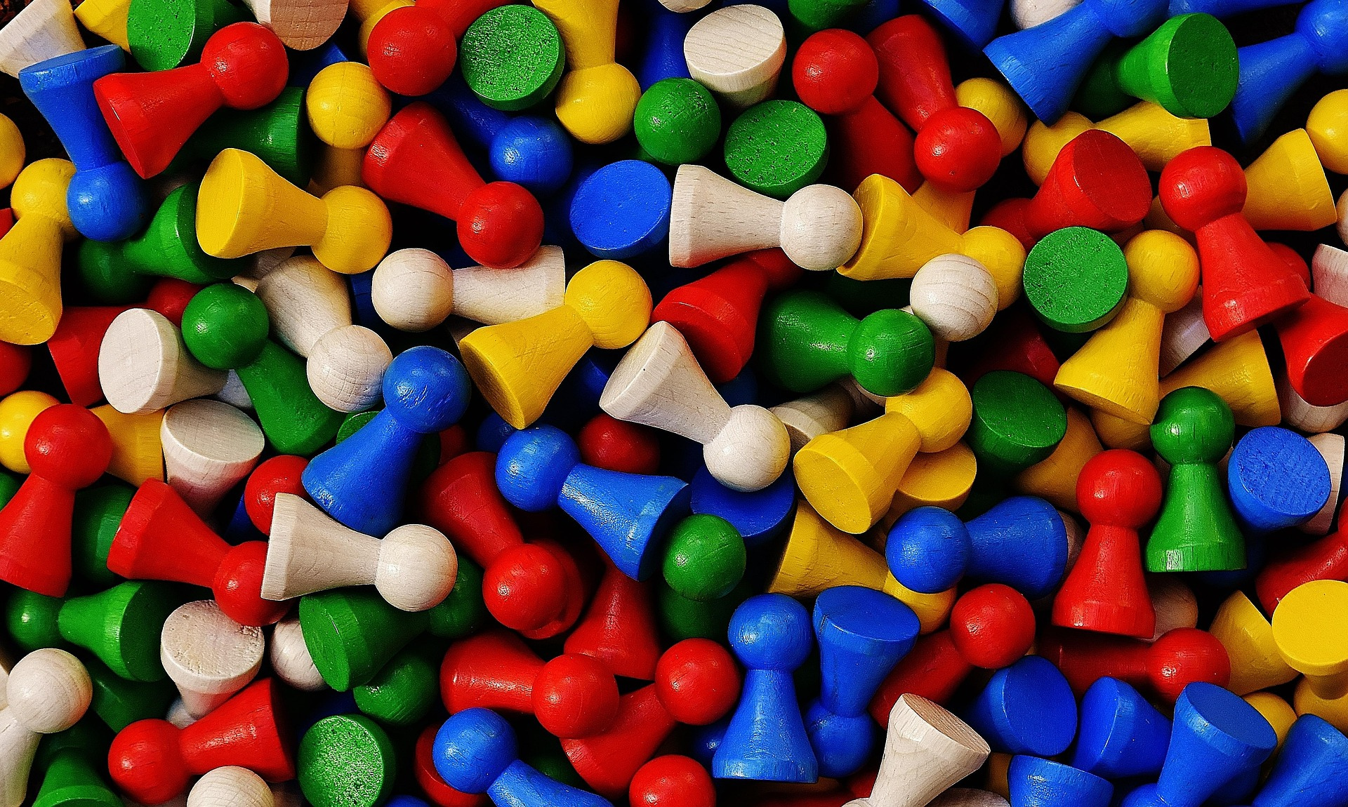 Colorful wooden game pieces resembling pawn tokens in red, blue, green, yellow, and natural wood colors scattered randomly.