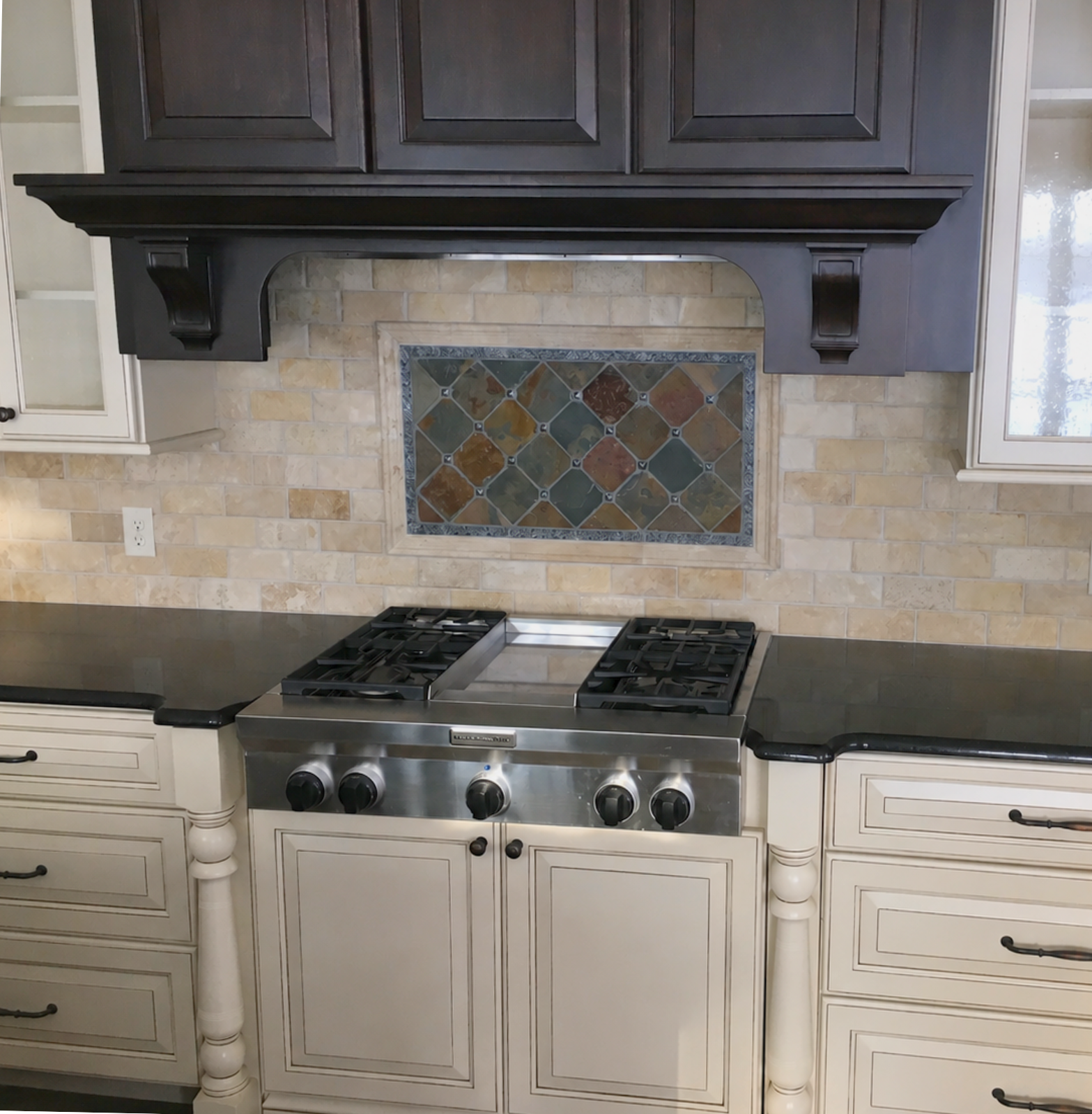 Kitchen with beige brick backsplash, decorative tile panel, black countertop, white cabinetry, and a stainless steel gas stove.