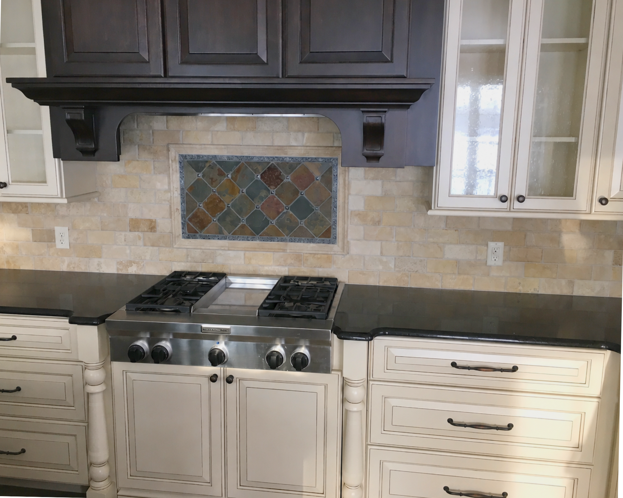 A kitchen with white cabinets, a granite countertop, a stove with four burners, and a backsplash with beige and multicolored tiles.
