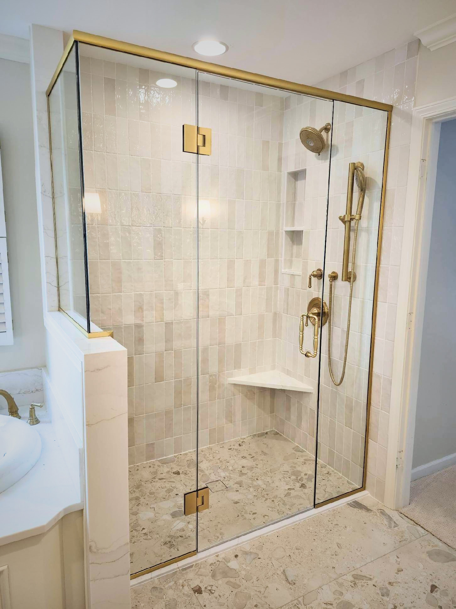 A glass-enclosed shower with gold fixtures and beige tiled walls and floor in a bathroom.