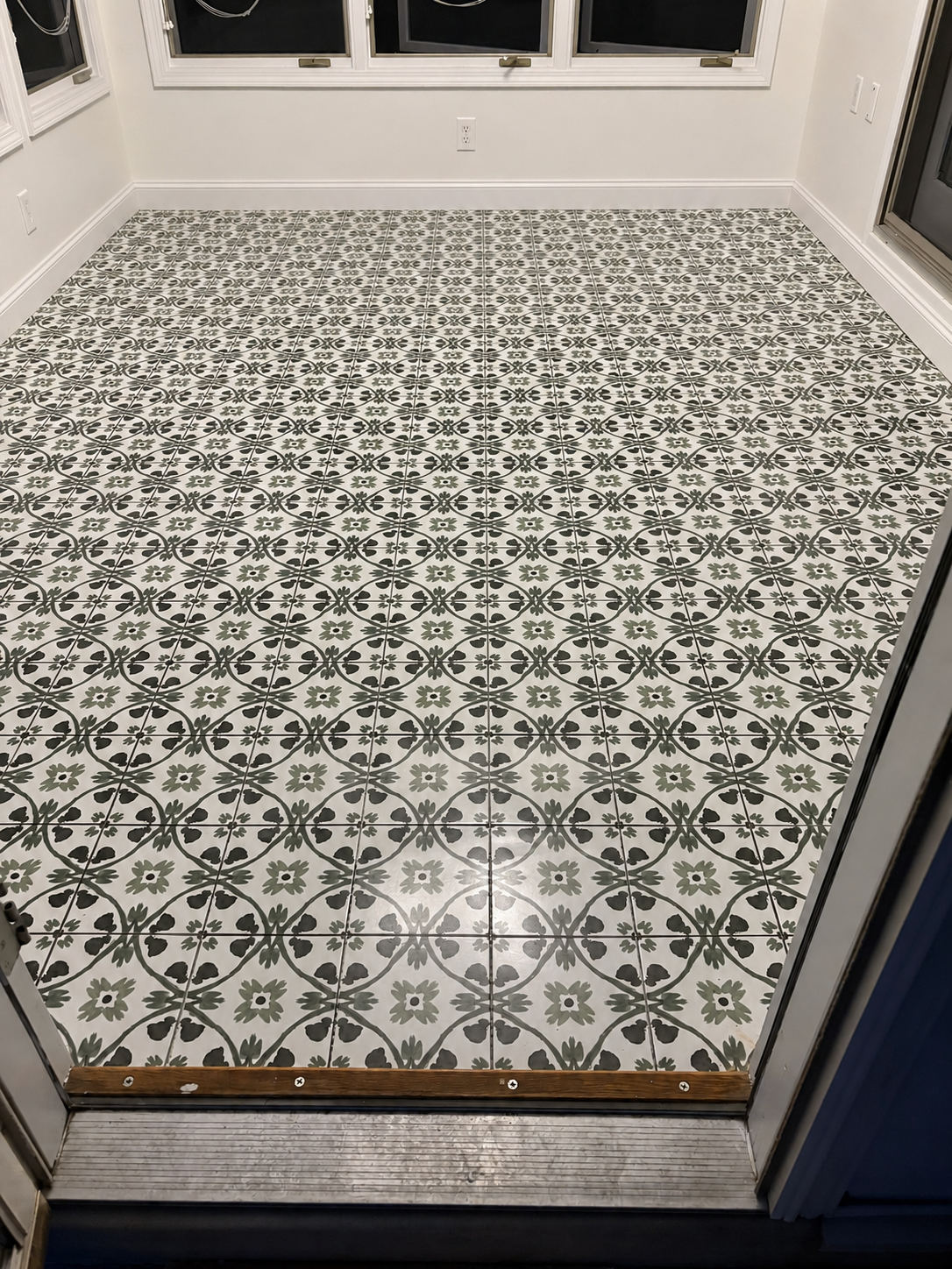 Interior view of a room with patterned tile flooring, white walls, and multiple windows, with a sliding glass door partially open.