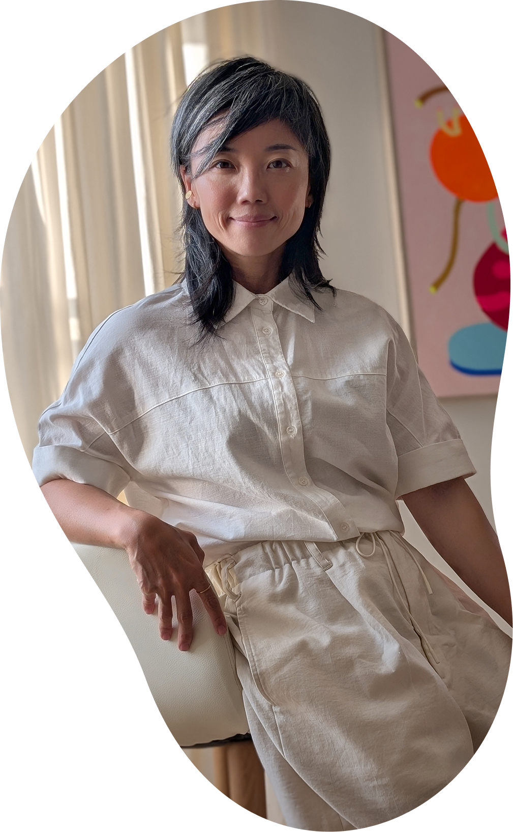 Photograph of Ruth Ong, life coach, in a cream living room with a colorful painting.