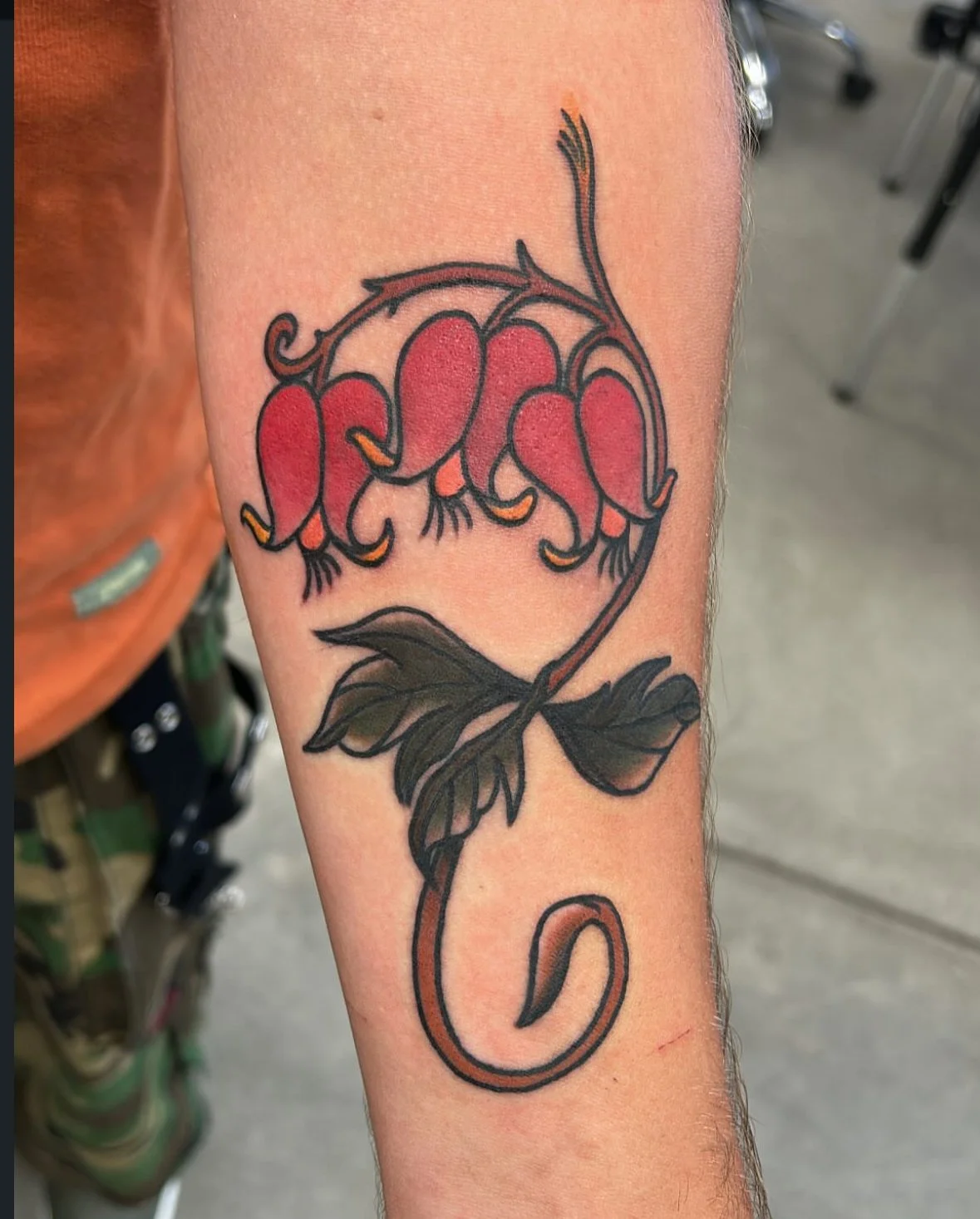 Tattoo of pink flowers with green leaves on a person's arm completed at our shop in Wheat Ridge, Colorado.