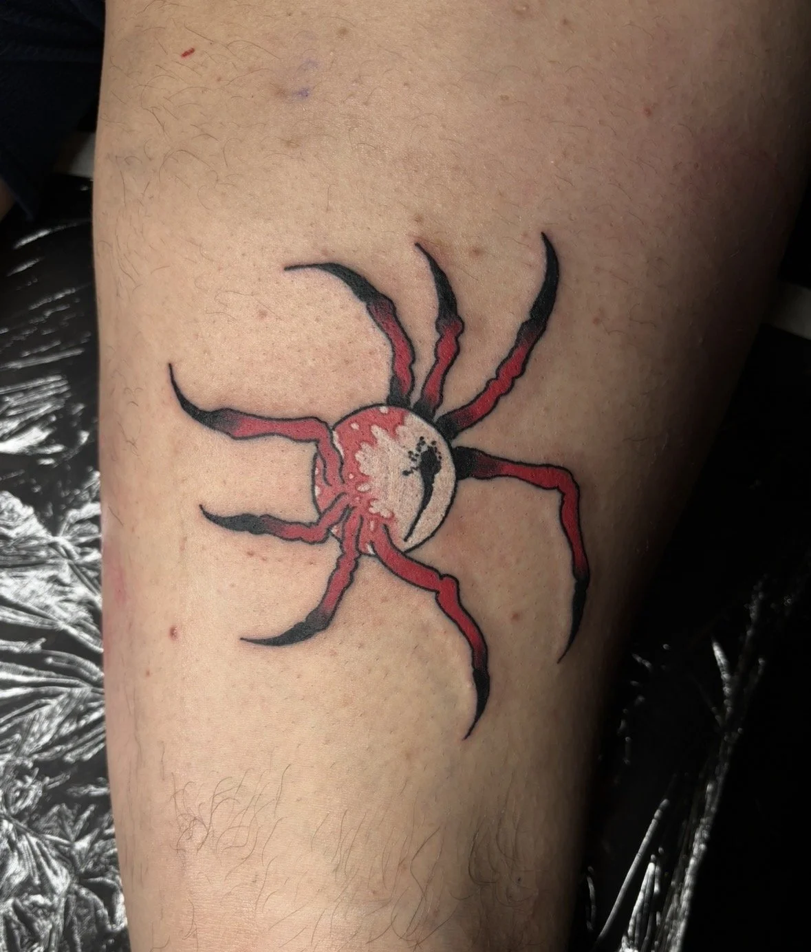 Tattoo of a red and black spider with a abstract eyeball for a body.