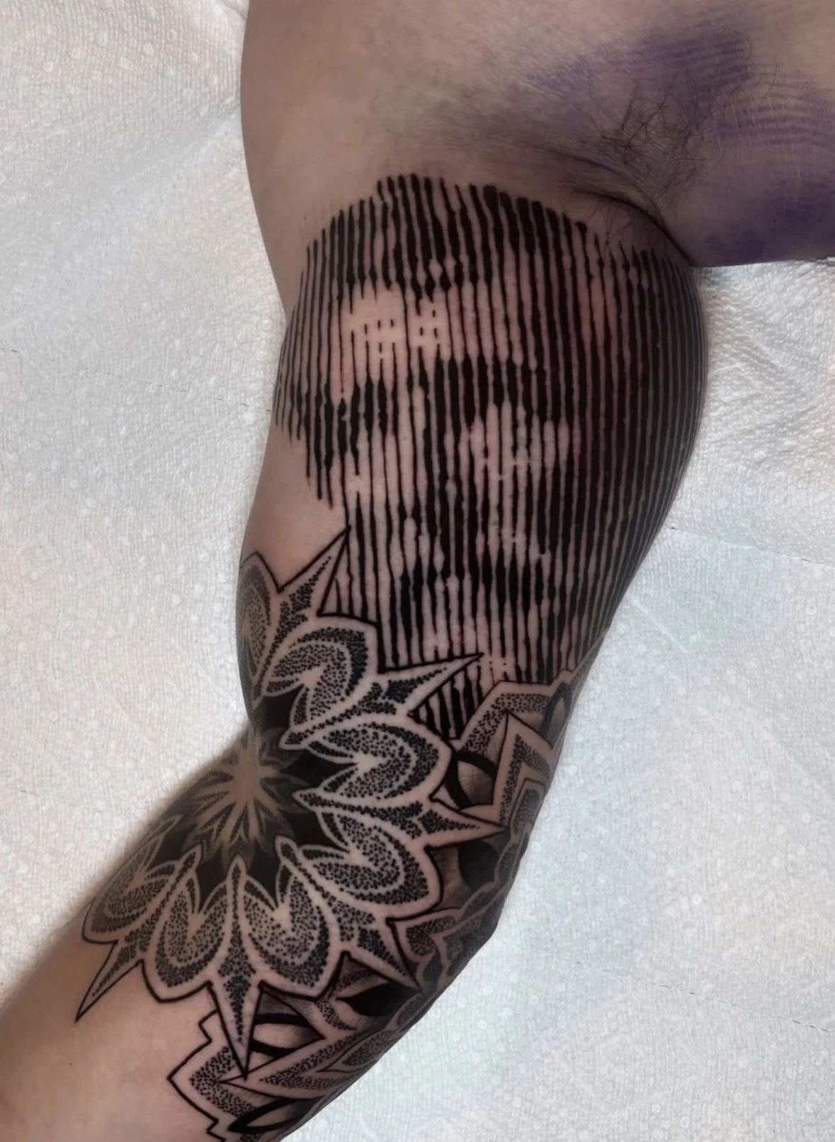 Abstract custom tattoo of a man's face on a person's upper arm, incorporated into a pattern of vertical lines and accompanied by geometric designs.