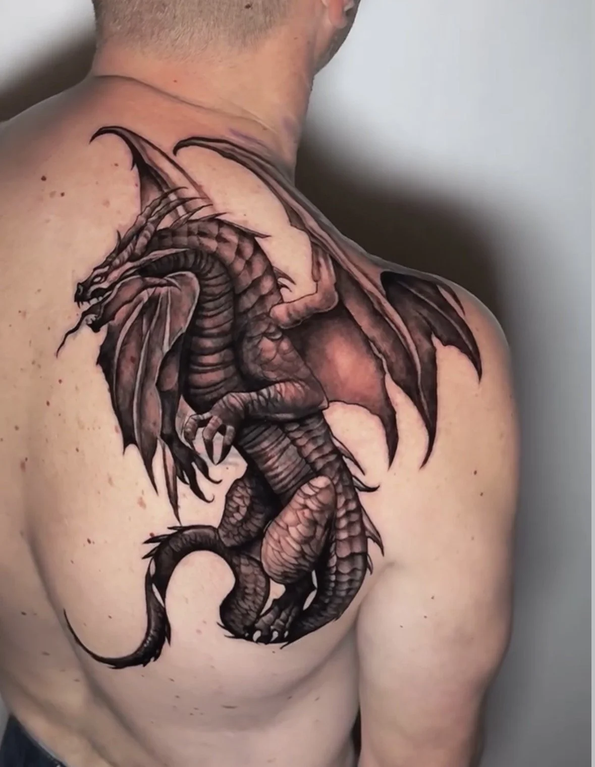 Tattoo of a detailed black and gray dragon on a person's back, shoulder and upper arm.