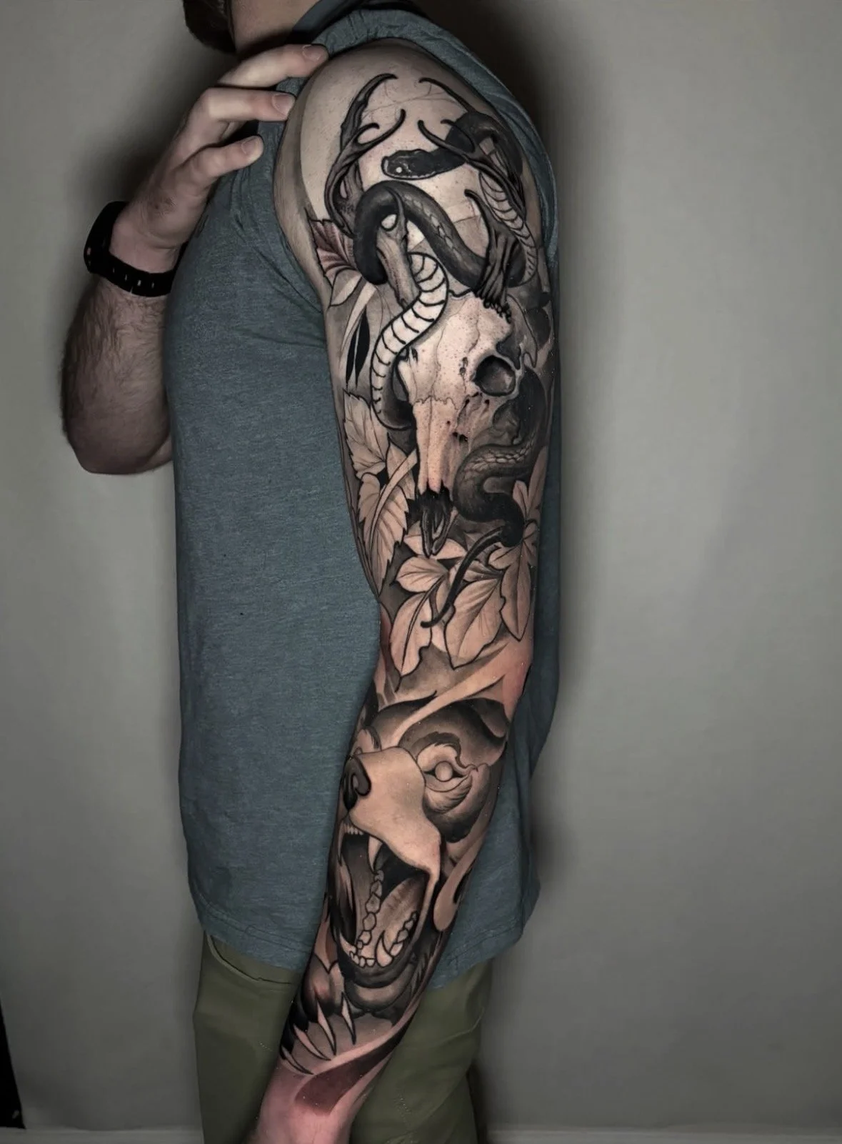A person with a large detailed black and gray tattoo sleeve featuring a snake, skull, and a roaring animal face on their arm.