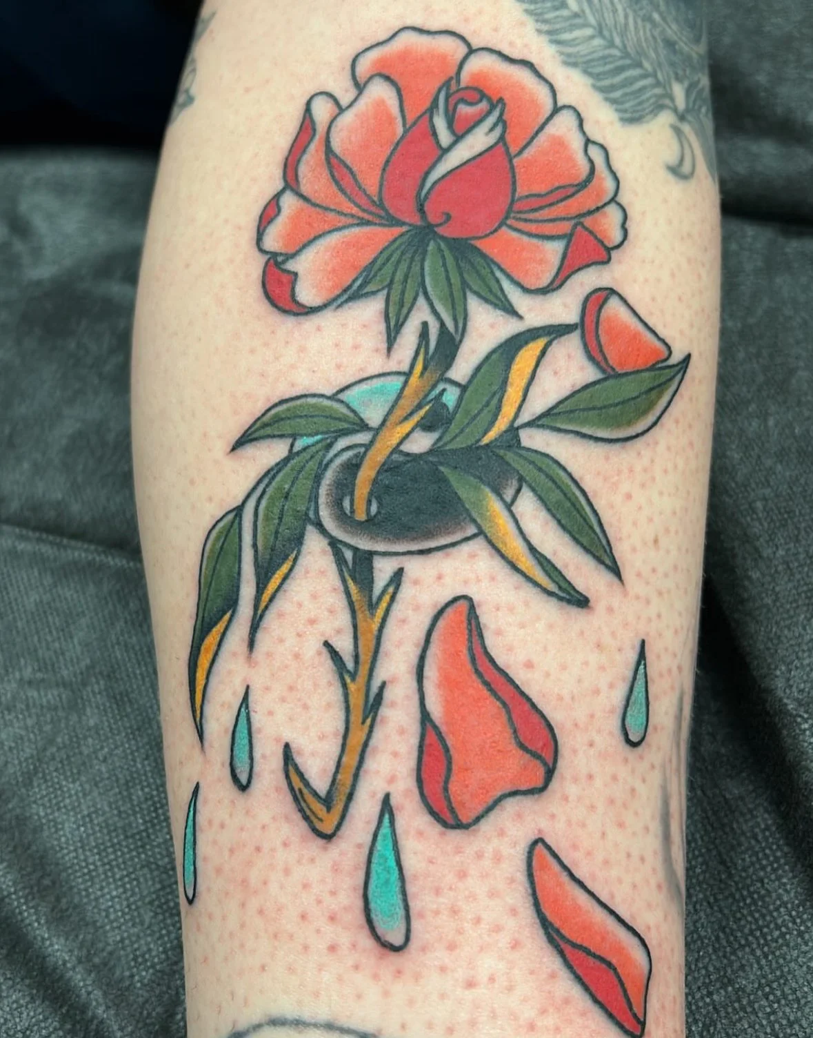 A colorful traditional style tattoo of a rose, surrounded by falling raindrops and flower petals, with bold black outlines and vivid colors.