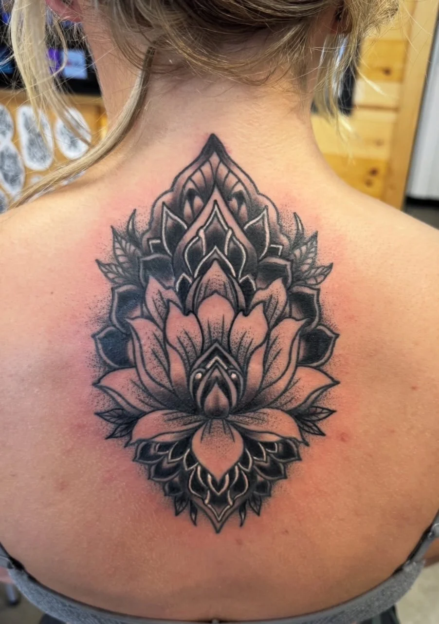 Black and gray lotus flower tattoo on person's upper back and neck.