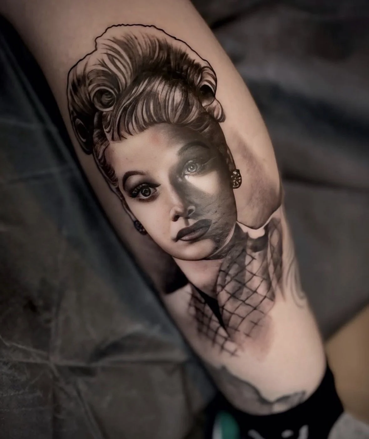 Tattoo of a woman's portrait, featuring a realistic face with styled hair and makeup, blending into a black and gray pattern, on a person's calf.