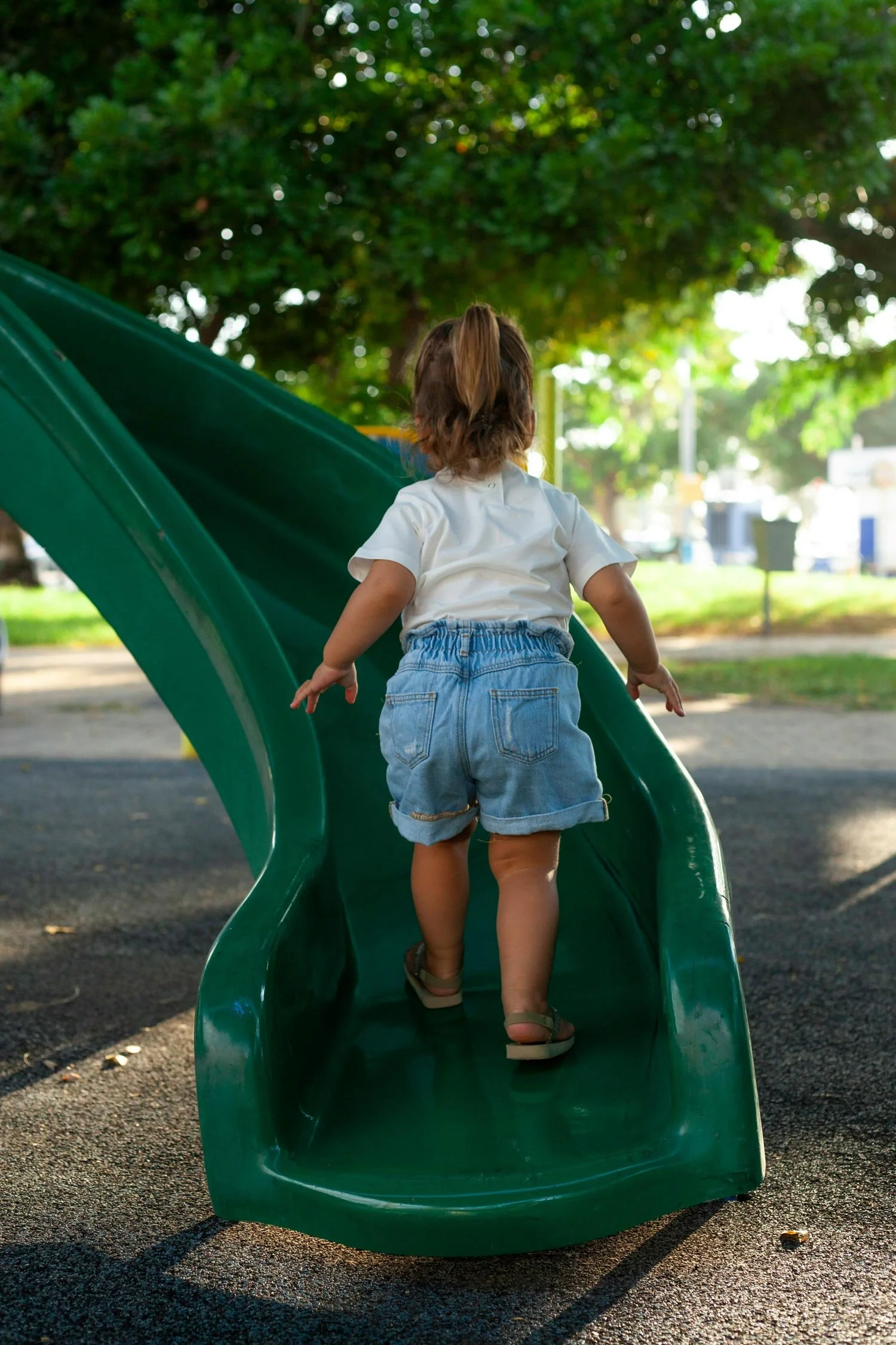 young girl climbing up a green slide