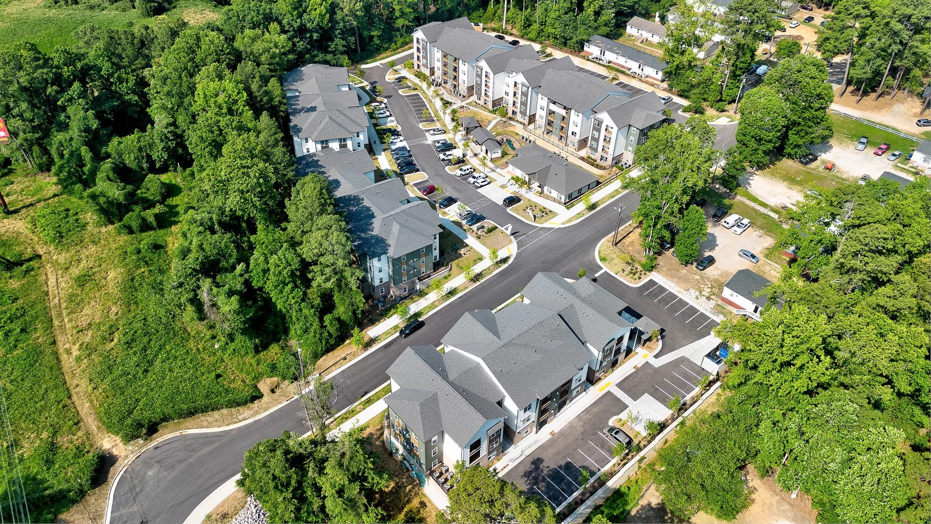 Aerial view of a residential apartment complex surrounded by trees and greenery, with parking lots and roads at The Pines at Peach Road in Raleigh, NC.
