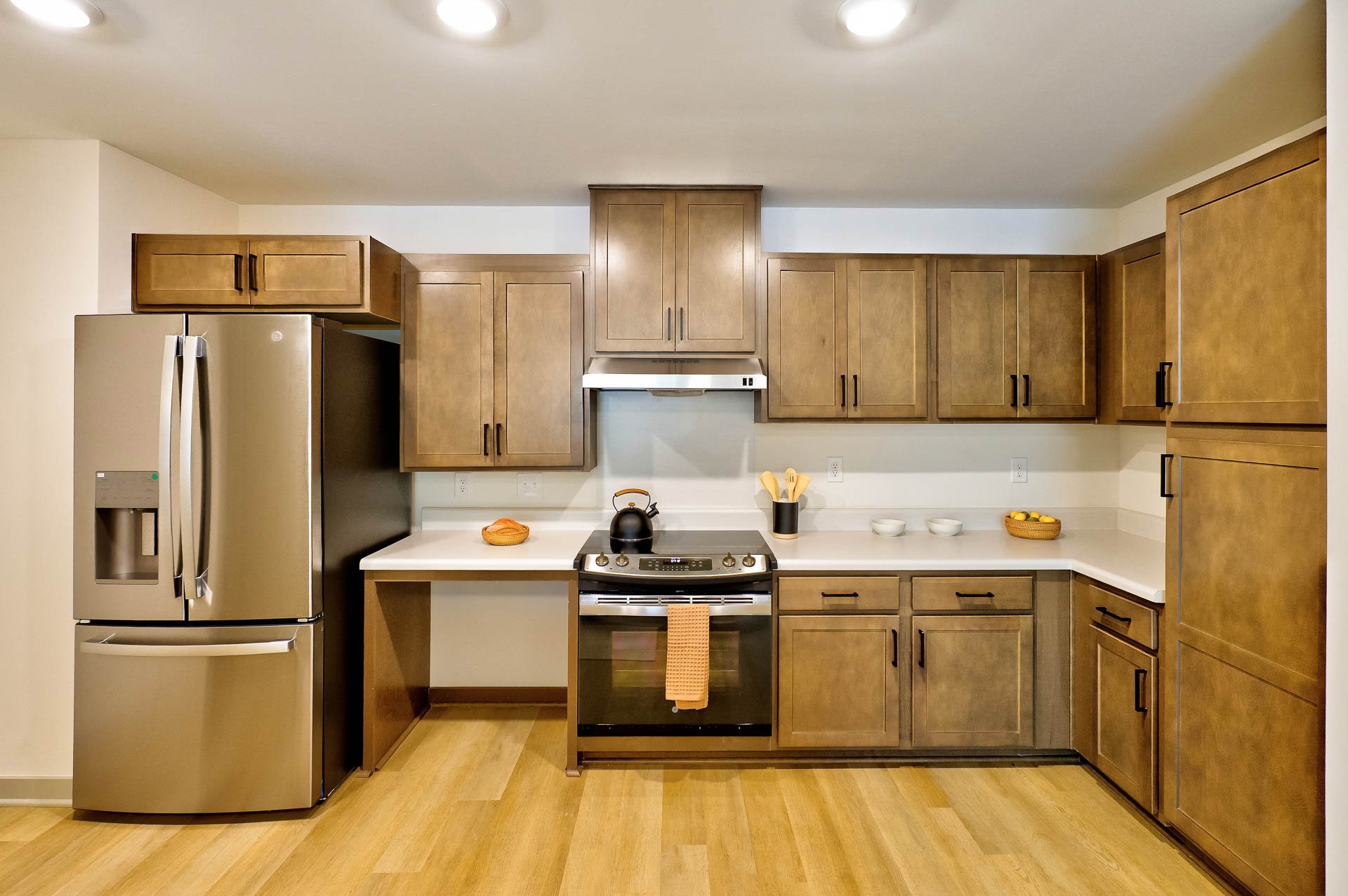Kitchen with wooden cabinets, stainless steel refrigerator, oven, and stovetop, decorated with bowls, a teapot, and a basket of lemons.