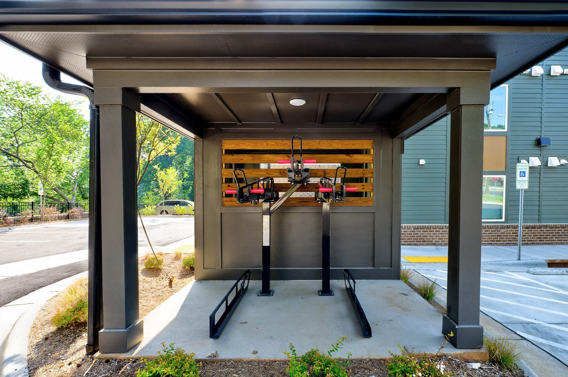 Outdoor gym equipment under a covered shelter with a wooden wall and green trees in the background at The Pines at Peach Road in Raleigh, NC.