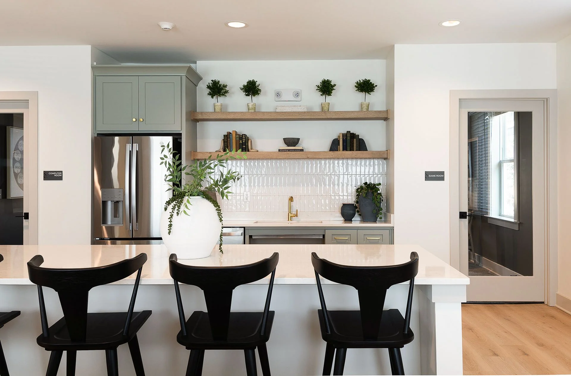 Community room kitchen with black bar stools and glossy white backsplash at The Pines at Peach Road
