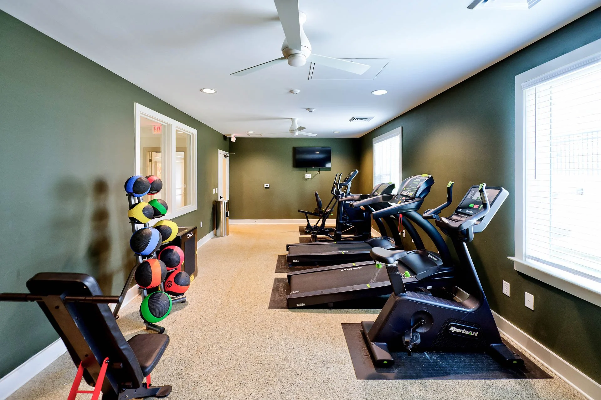 Fitness room with green walls, carpeting, windows with blinds, and treadmill exercise machines.