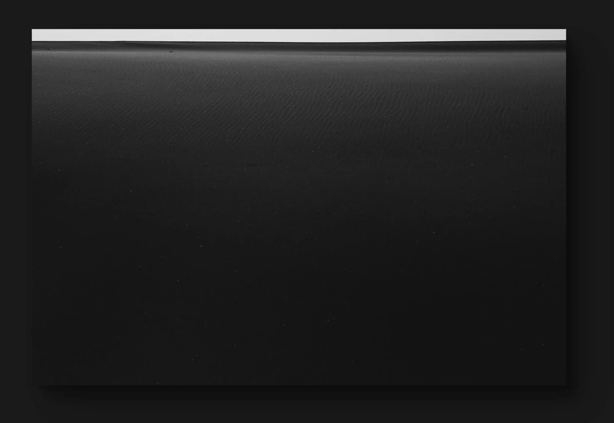 Une image monochrome représentant une surface sableuse avec un horizon au loin, composée de deux bandes horizontales blanches au sommet