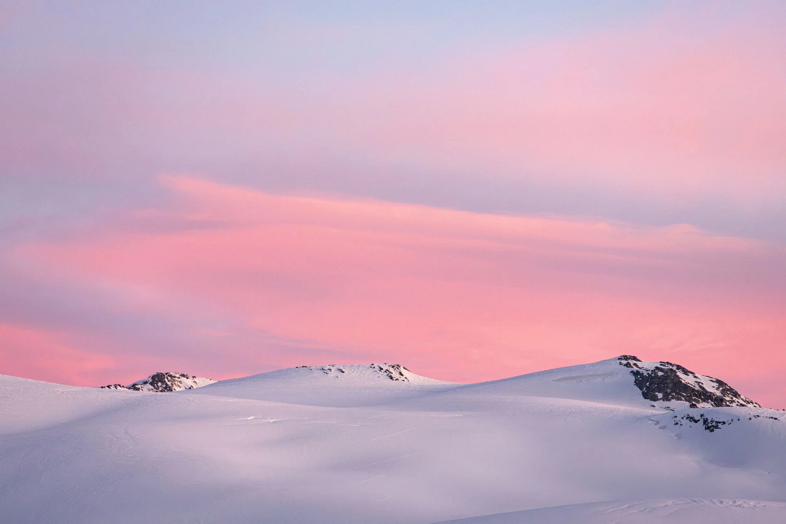Ciel pastel rose et violet au-dessus de montagnes enneigées.