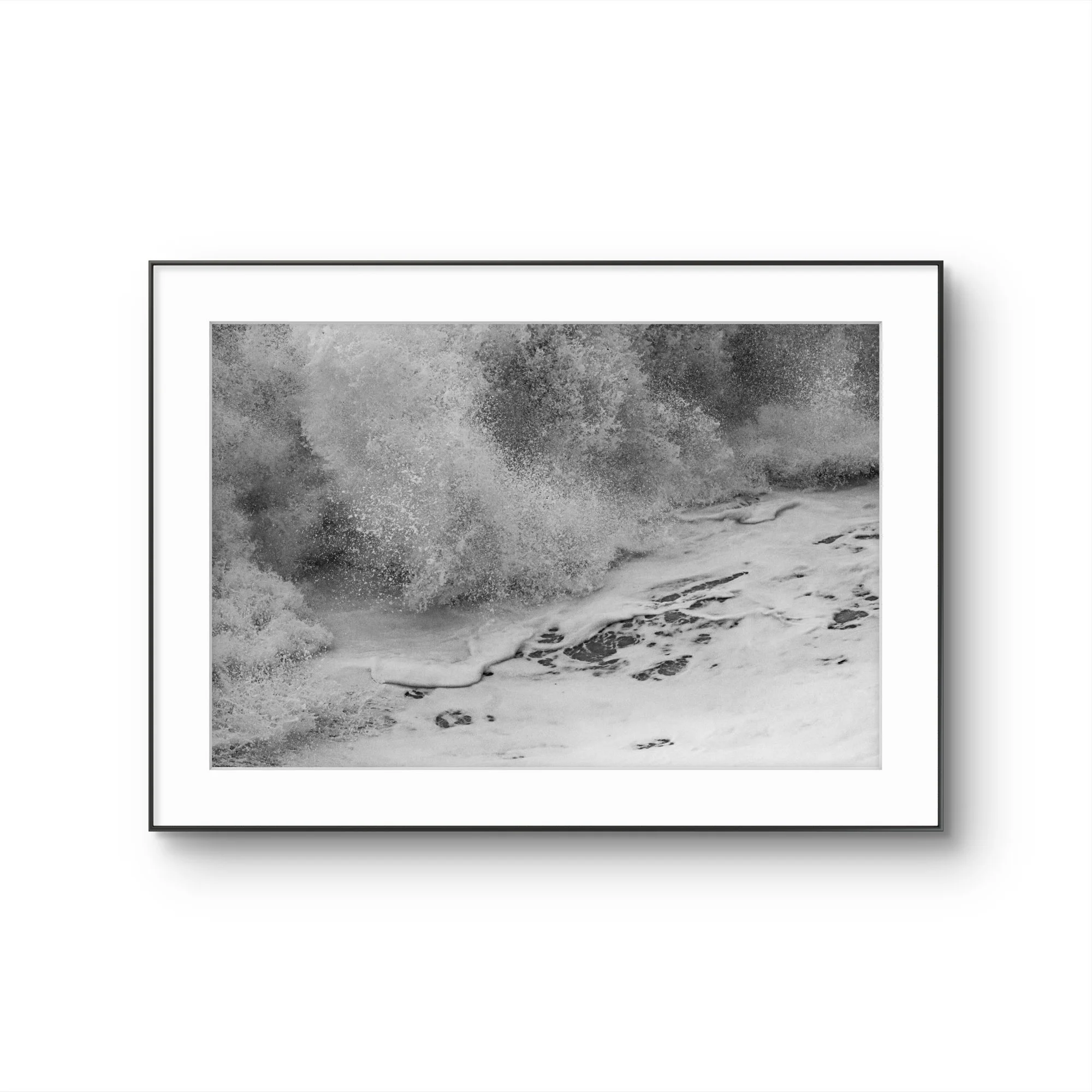 Une photographie en noir et blanc d'une mer avec des vagues se brisant sur la plage, capturée au bord de l'eau.