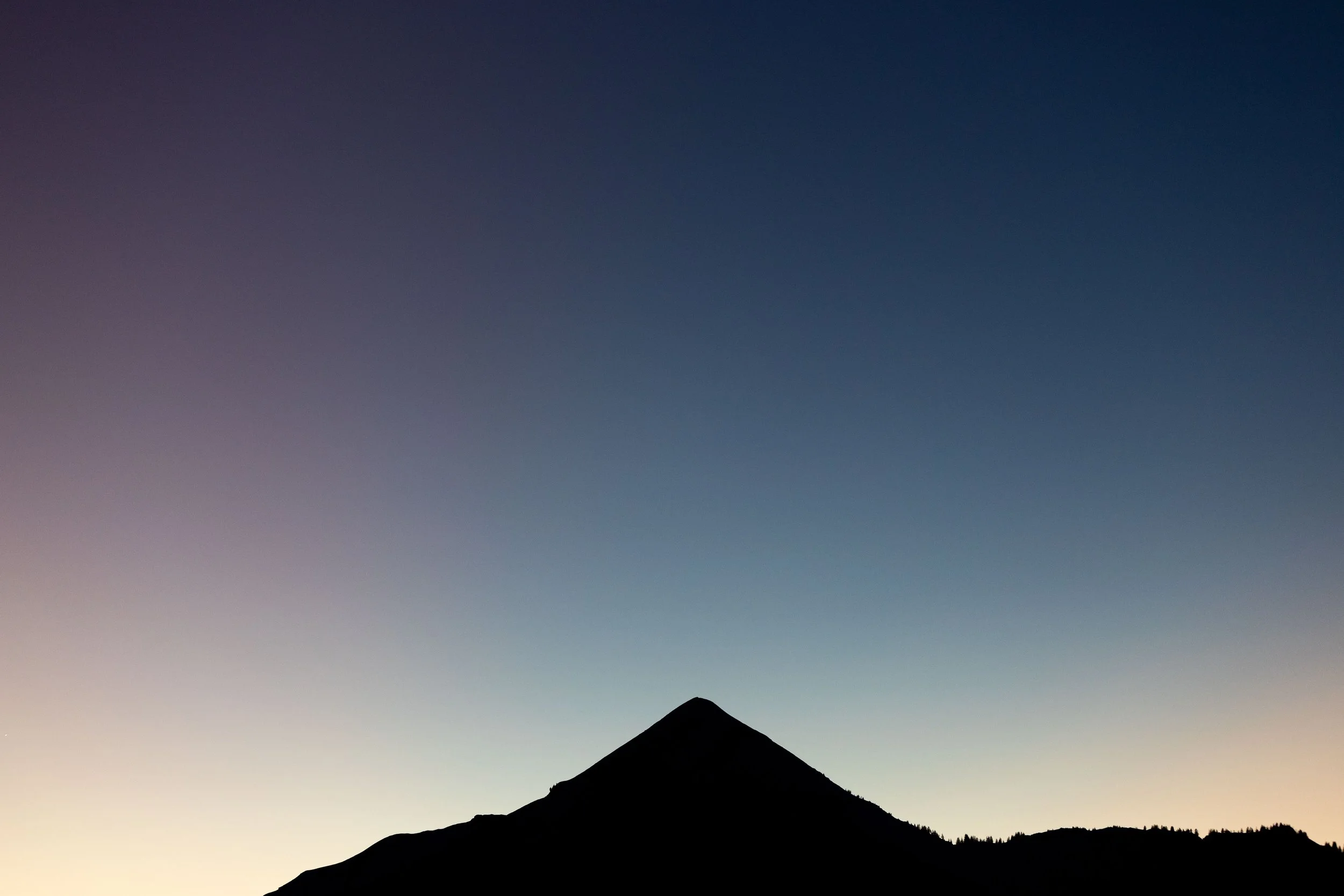 Silhouette d'une montagne contre un ciel à dégradé de couleurs au coucher du soleil.