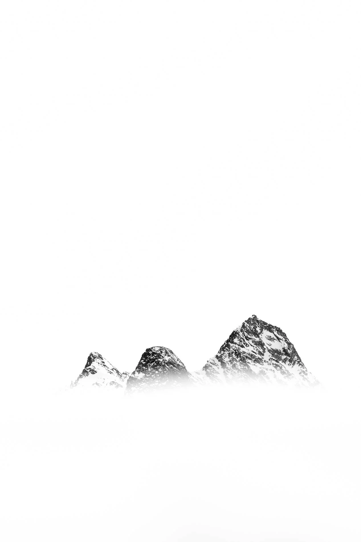 Montagnes enneigées avec un sommet pointu et plusieurs sommets arrondis, sous un ciel blanc.