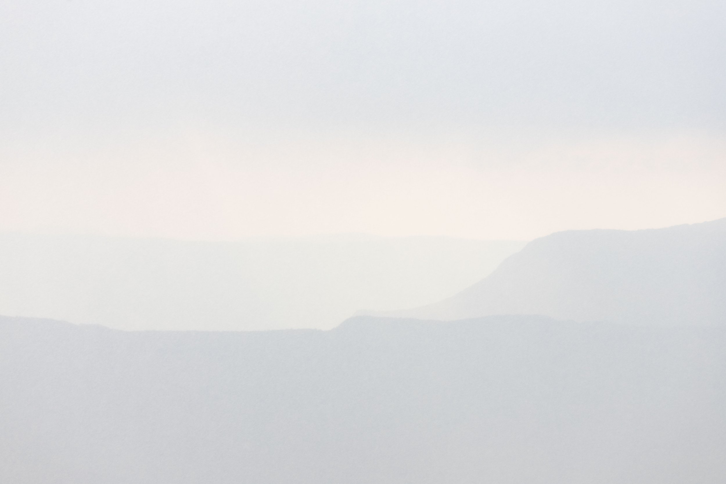 Une scène brumeuse avec des montagnes ou des collines lointaines observées à travers la brume ou le brouillard léger.