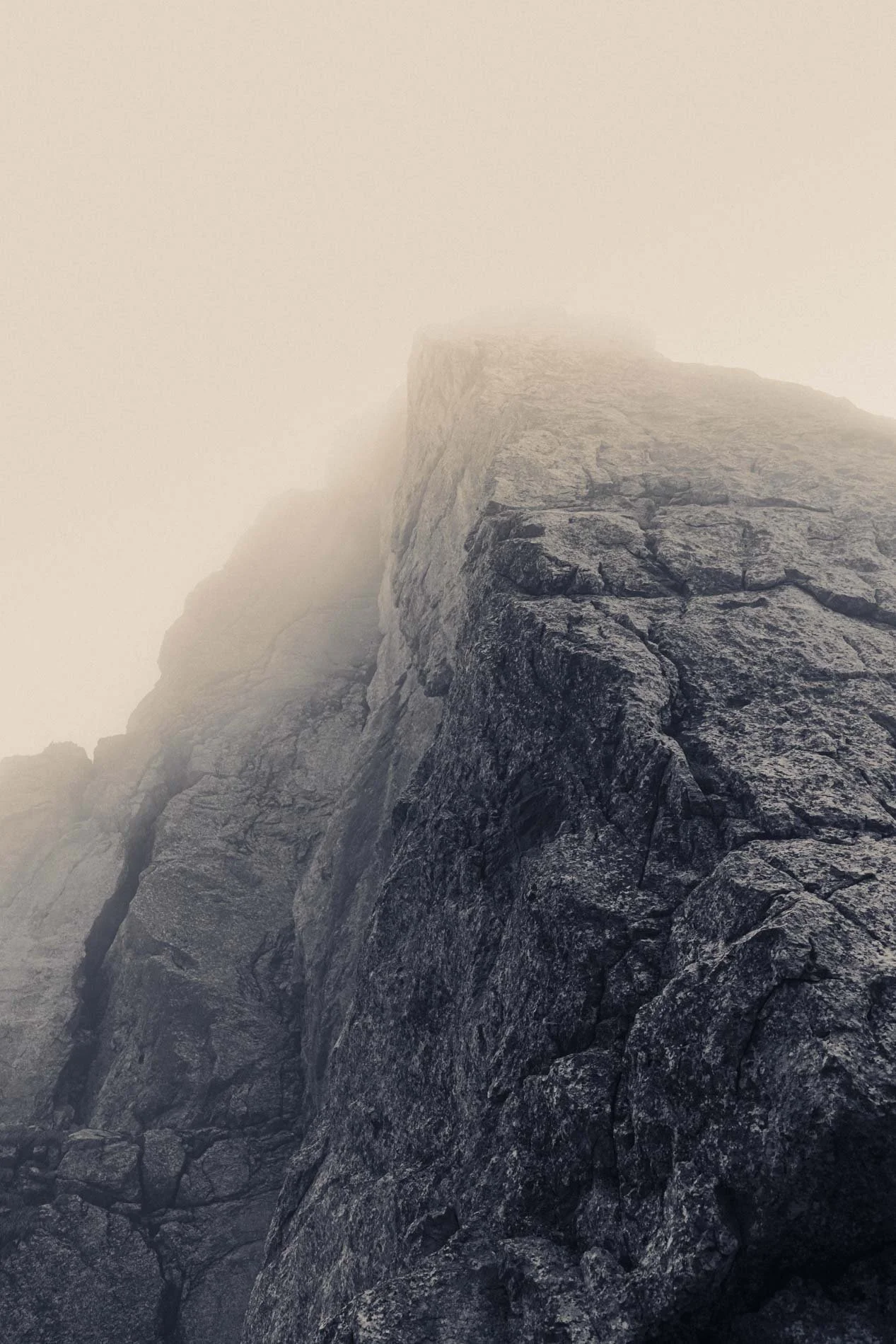 Une roche escarpée et rocheuse recouverte de brouillard ou de nuages, créant une ambiance mystérieuse et froide. La photo semble avoir été prise en haute montagne ou dans un environnement très isolé.