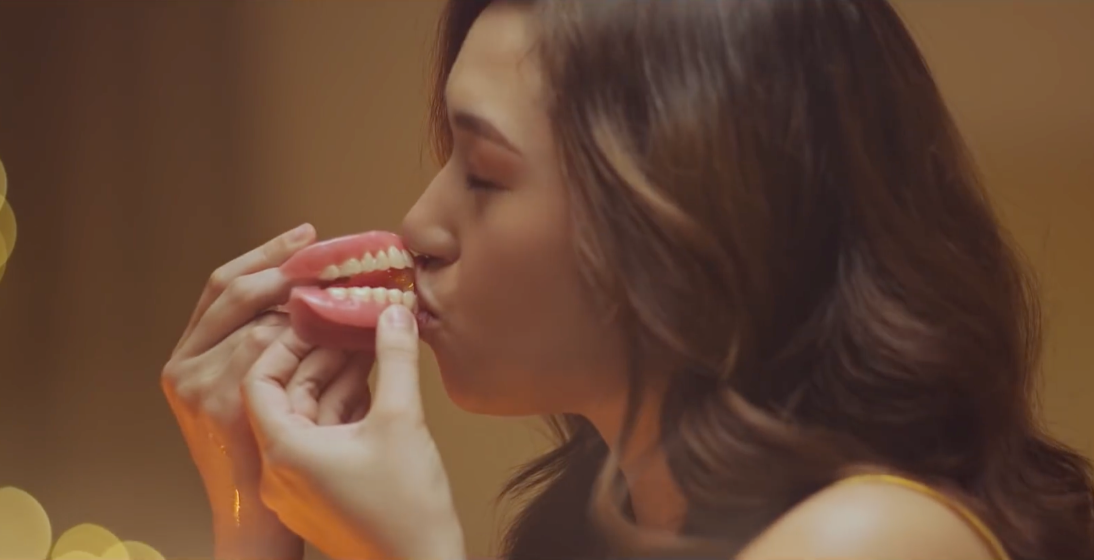 A woman with brown hair is kissing a pair of dentures