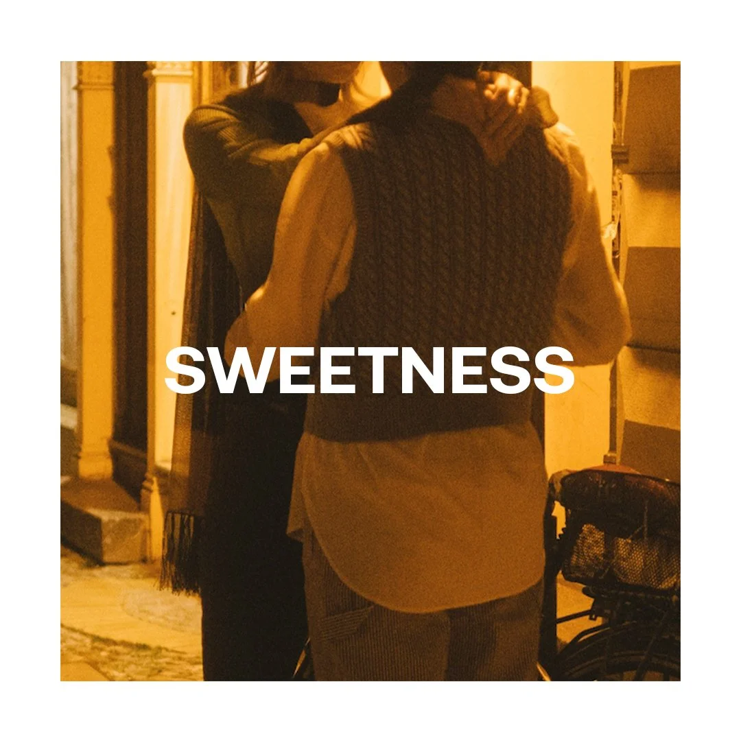 Two women standing close together outdoors at night, one with their arm around the other, with the word 'SWEETNESS' overlaid in white text.