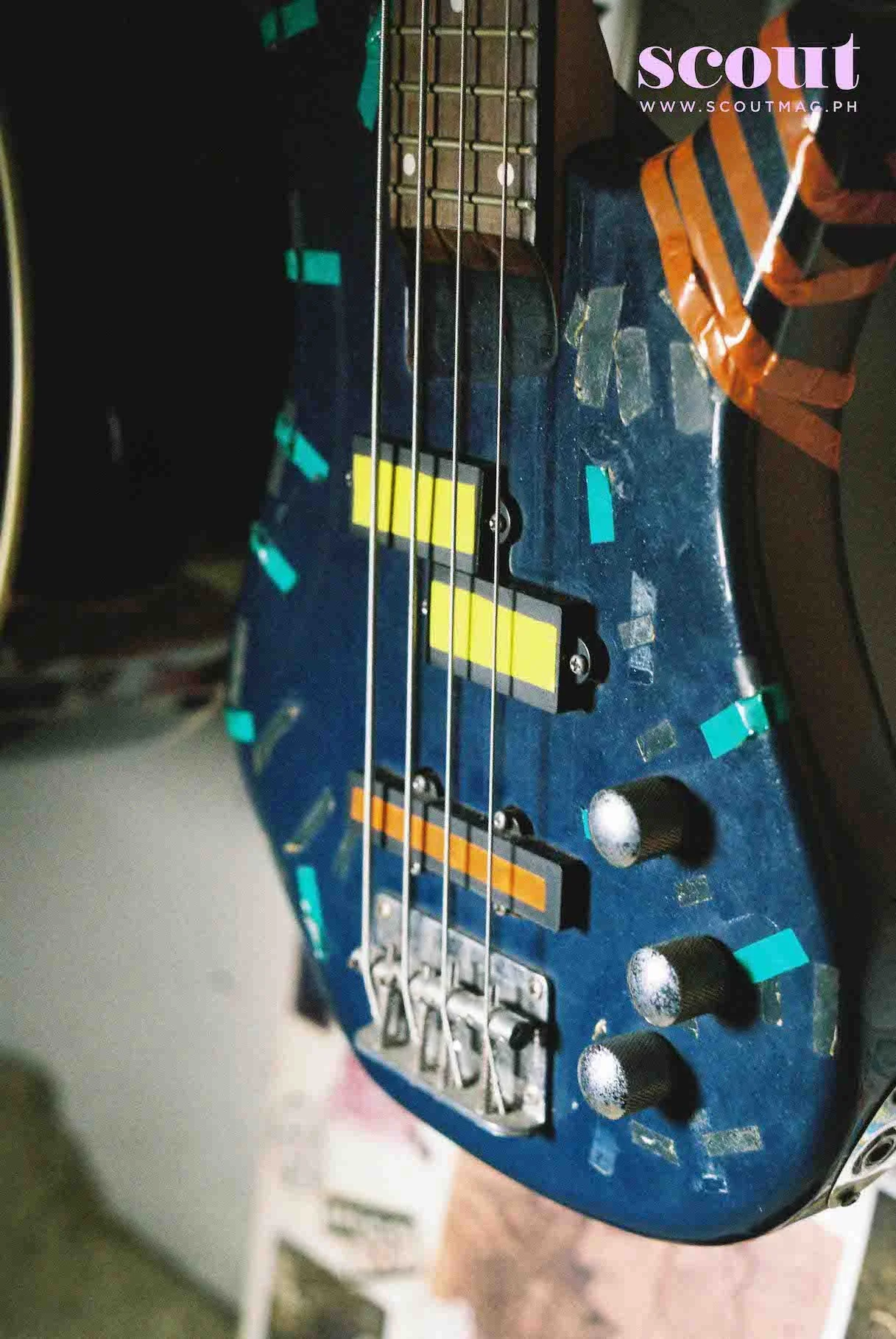 Close-up of an electric guitar headstock with tuning pegs and electric pickups, marked with multiple colored tape pieces.