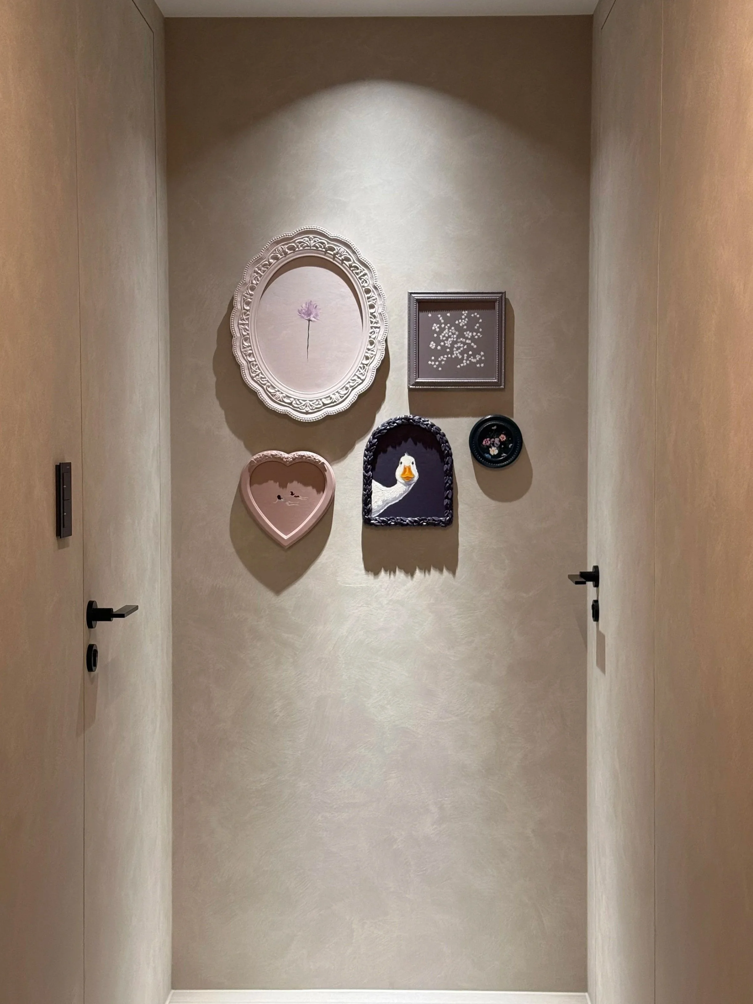 Decorative wall with framed artwork, including a pink flower and a duck, in a hallway
