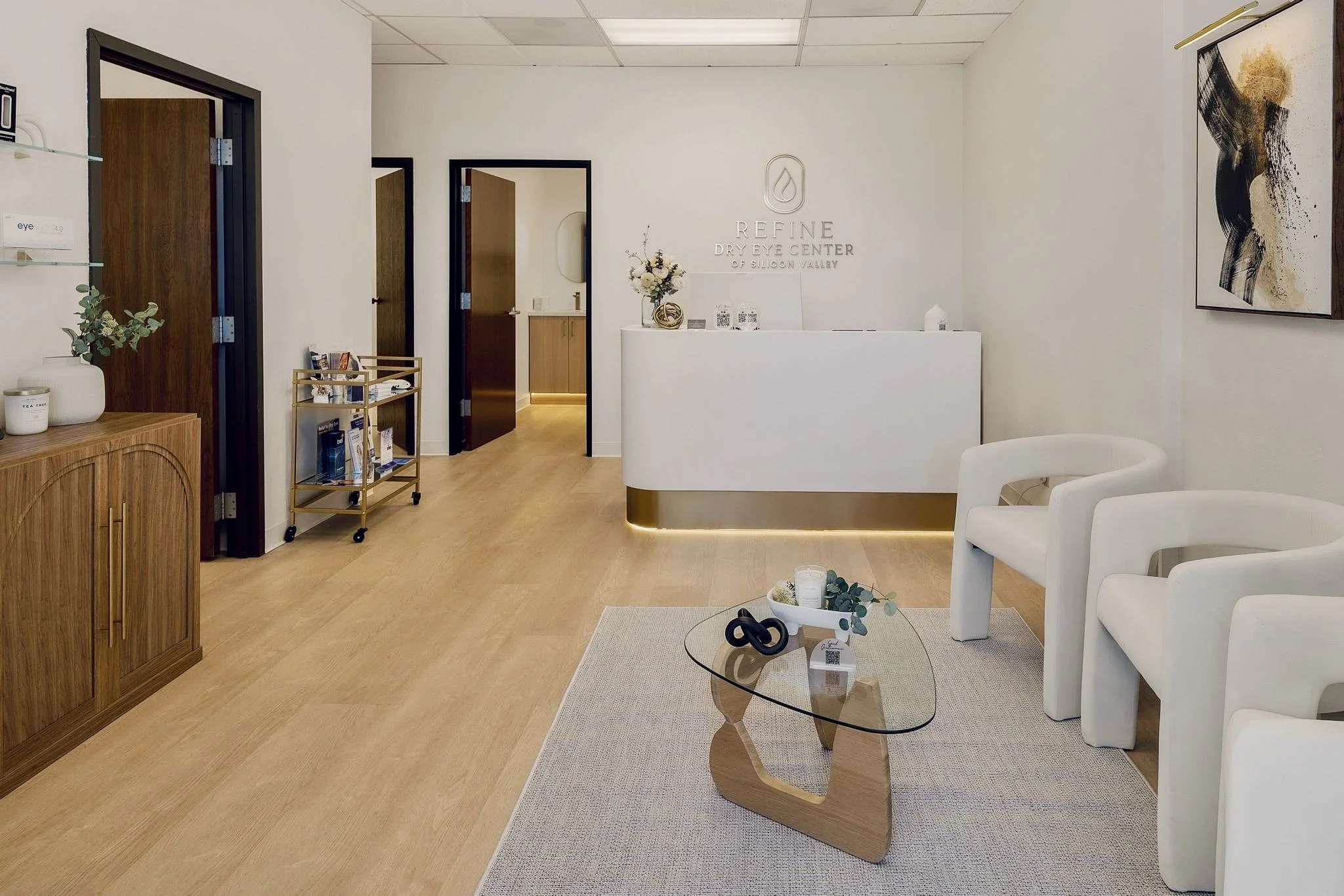 Interior of a modern dry eye center with a reception desk, white chairs, artwork on the wall, and decorative plants.