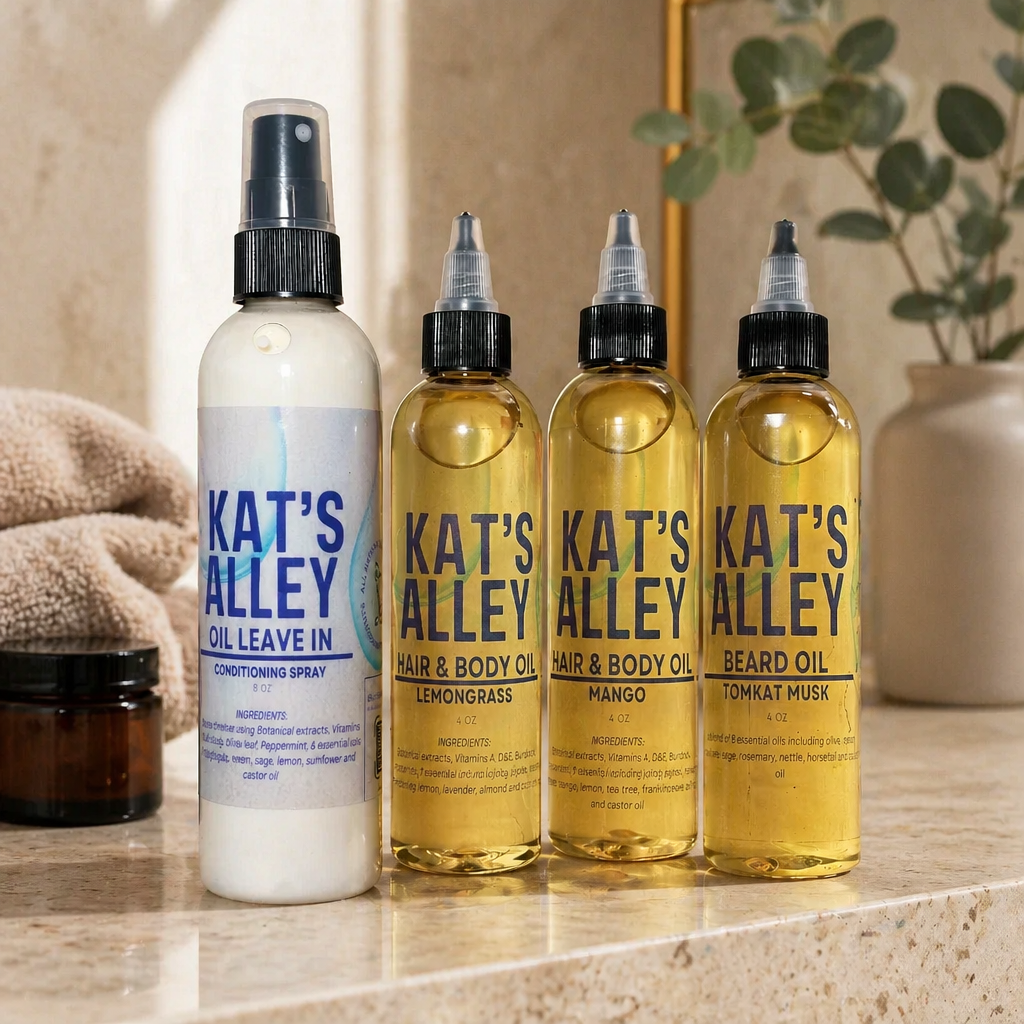 Four bottles of personal care products, including a white spray bottle labeled 'KAT'S ALLEY OIL LEAVE IN CONDITIONING SPRAY' and three clear bottles labeled 'KAT'S ALLEY HAIR & BODY OIL' in lemon grass, mango, and tomkat musk scents.