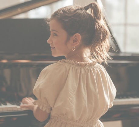 Young girl with a ponytail playing the piano in a sunlit room.
