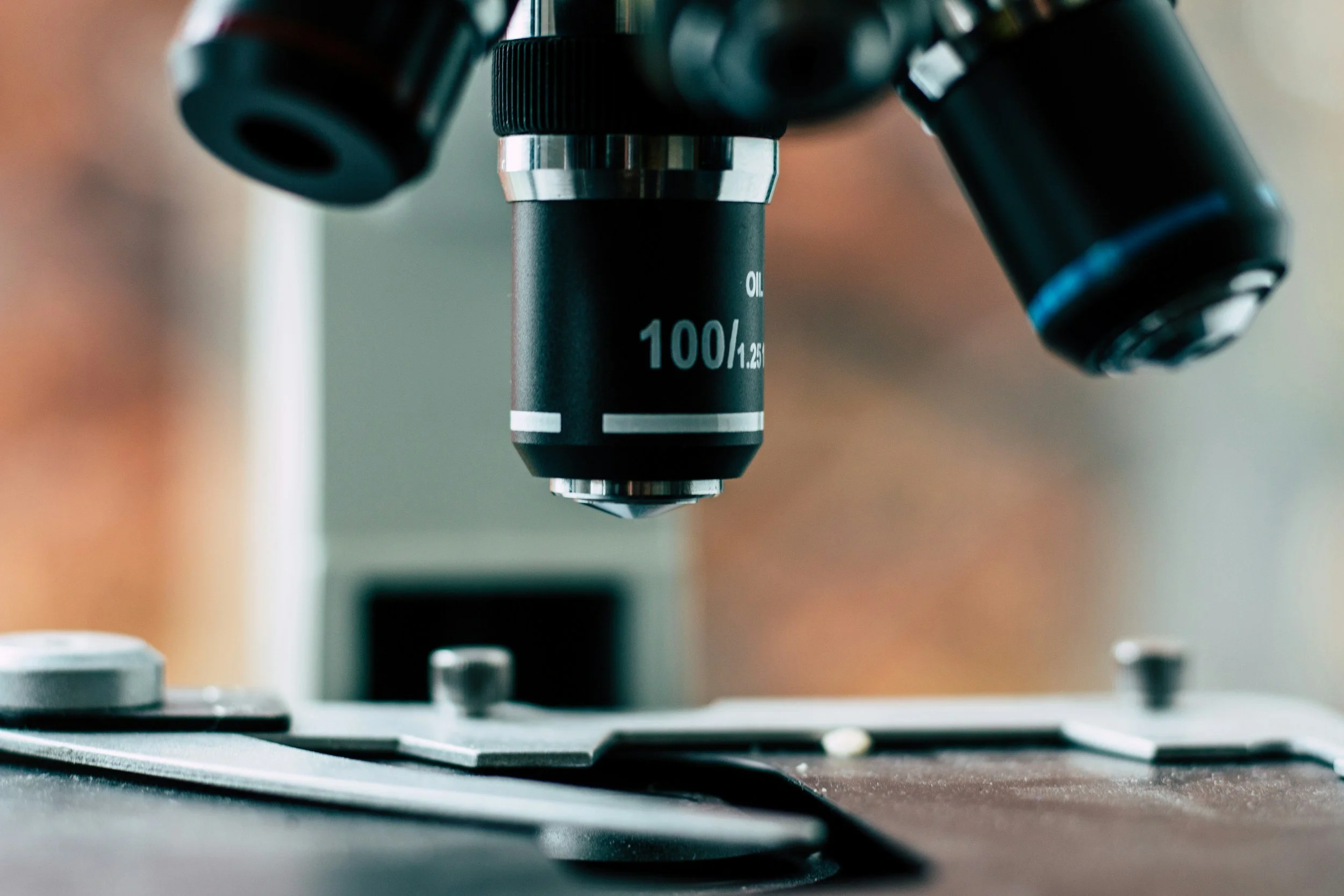 Close-up of a microscope focusing on a sample slide, with the objective lens marked 100x.