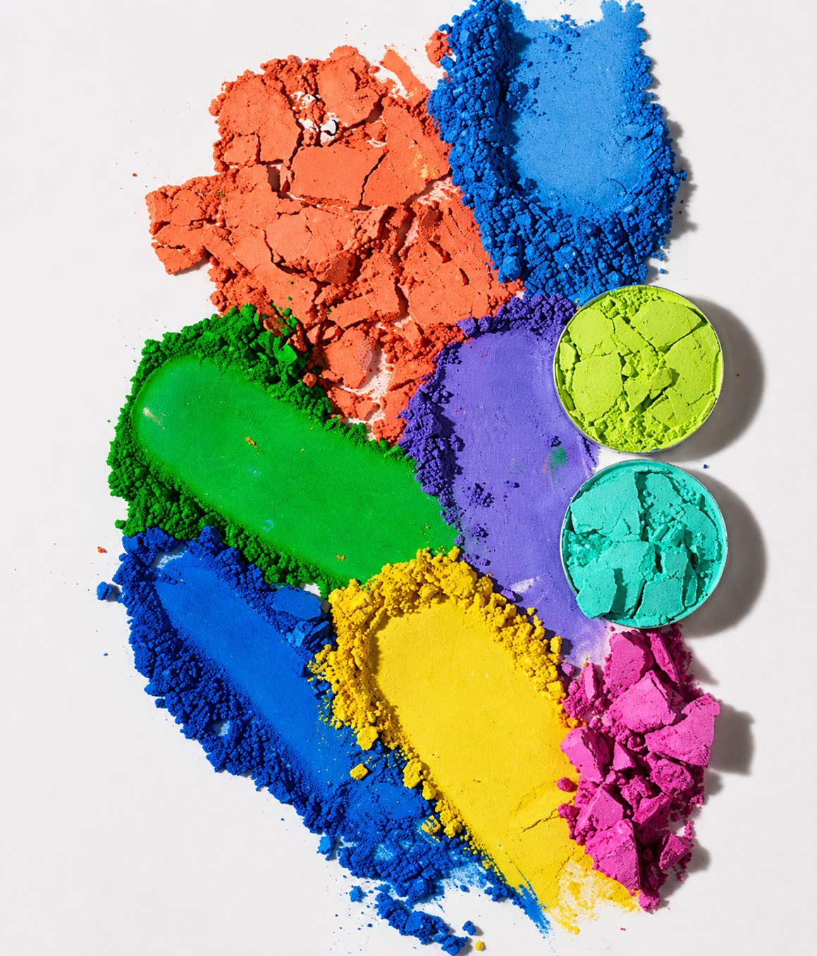 Colorful powder pigments in red, blue, green, purple, yellow, and pink on white background, with some in small containers.